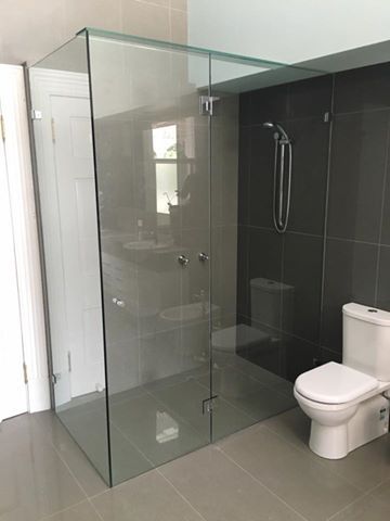 Glass shower enclosure in a modern bathroom with gray walls and a white toilet.