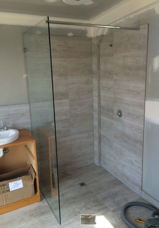 A modern, glass-walled shower with beige tile walls and floor.