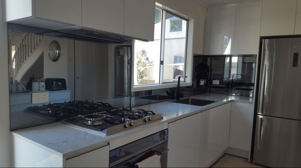 Modern white kitchen with stainless steel appliances, stove, and window.
