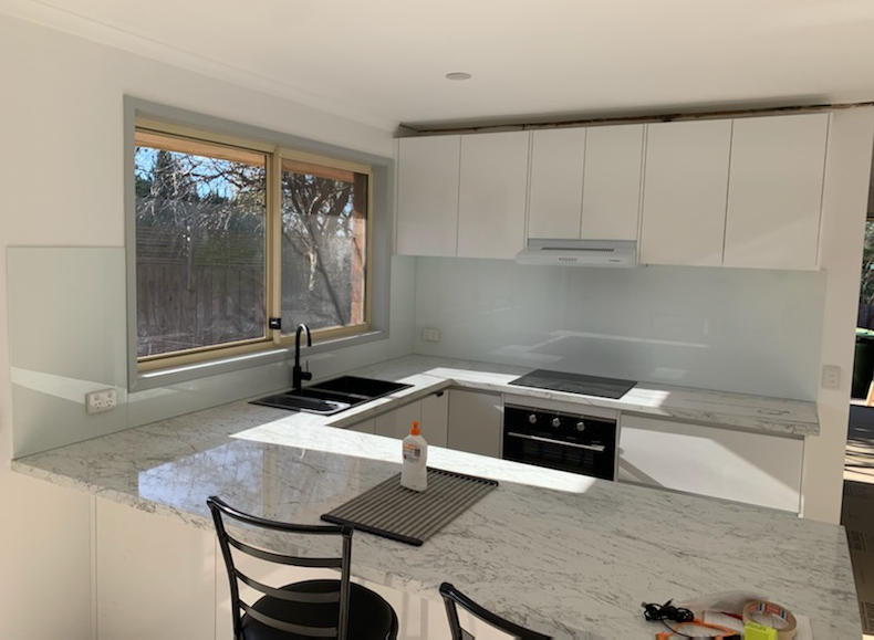 Modern white kitchen with granite countertops, window, and black appliances.