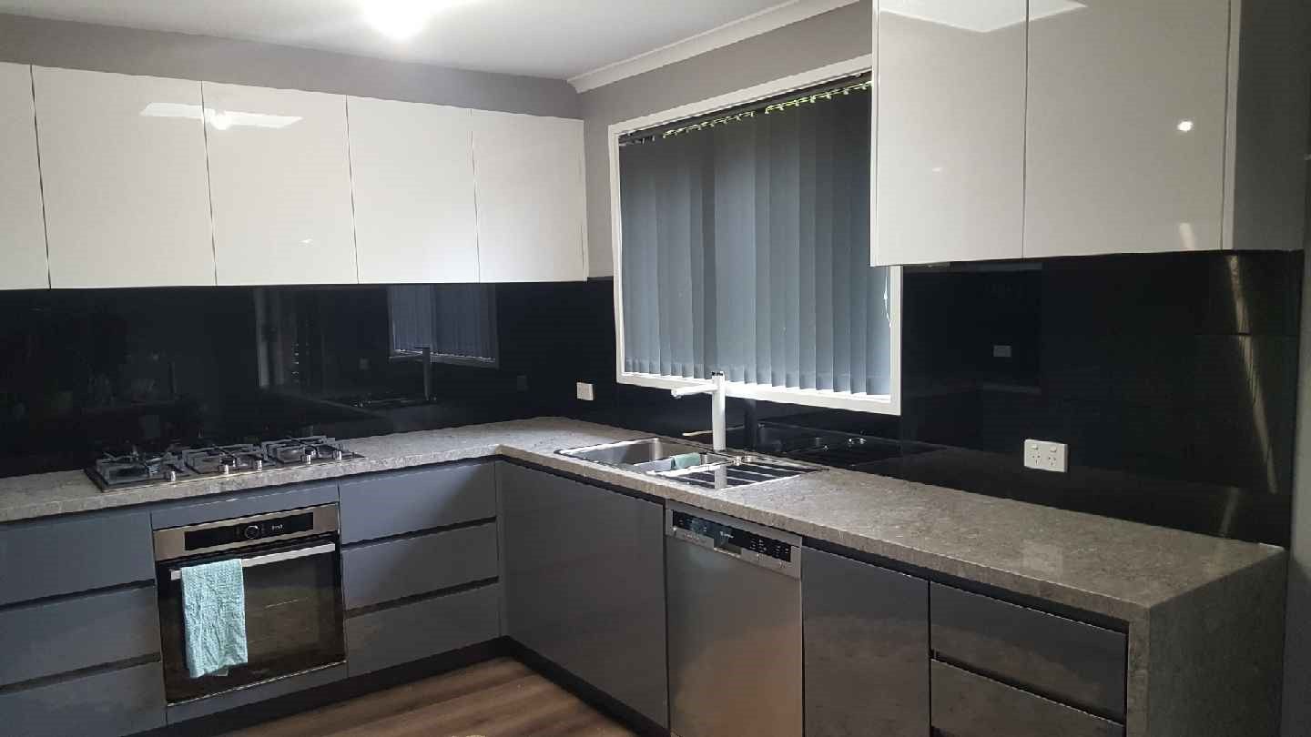 Modern gray and white kitchen with stainless steel appliances and black backsplash.