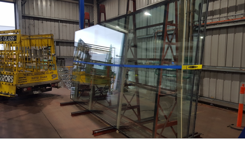 Large glass pane secured by a blue strap on a metal frame, yellow truck in the background.