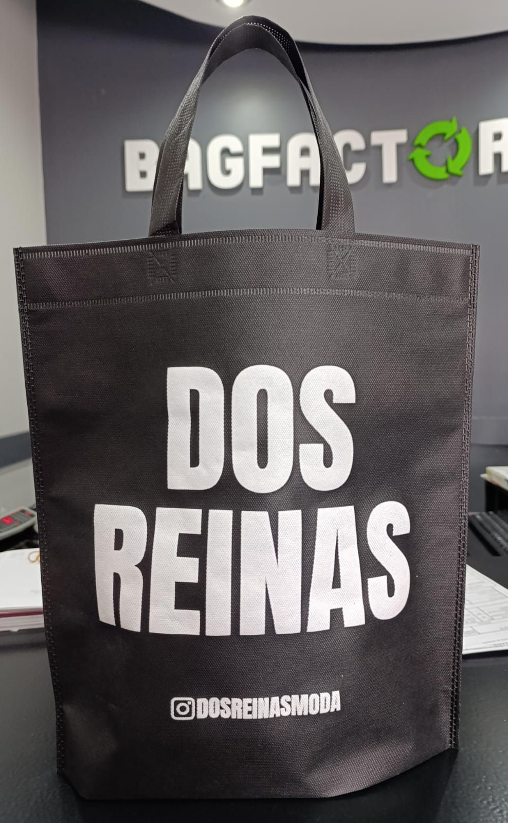 Una bolsa de mano negra con las palabras "dos reinas" está sobre una mesa.