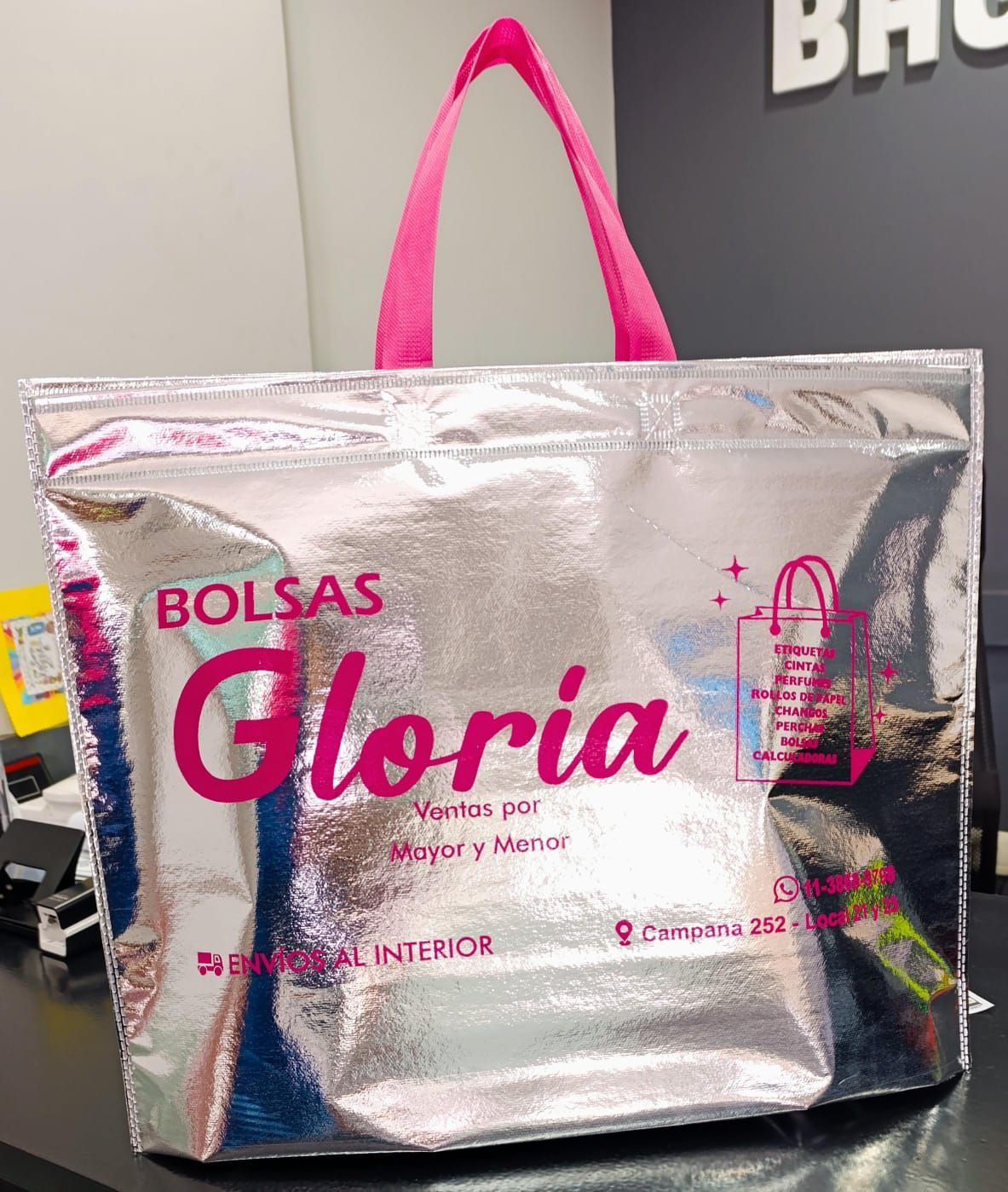Un bolso plateado con un asa rosa está sobre una mesa.