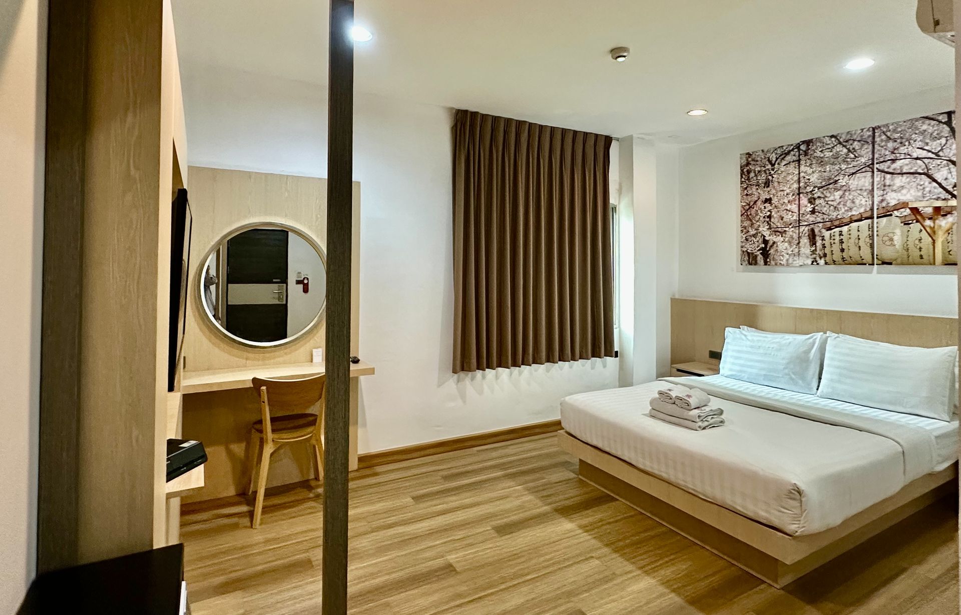 Hotel room with bed, desk, mirror, artwork, and window with curtains.