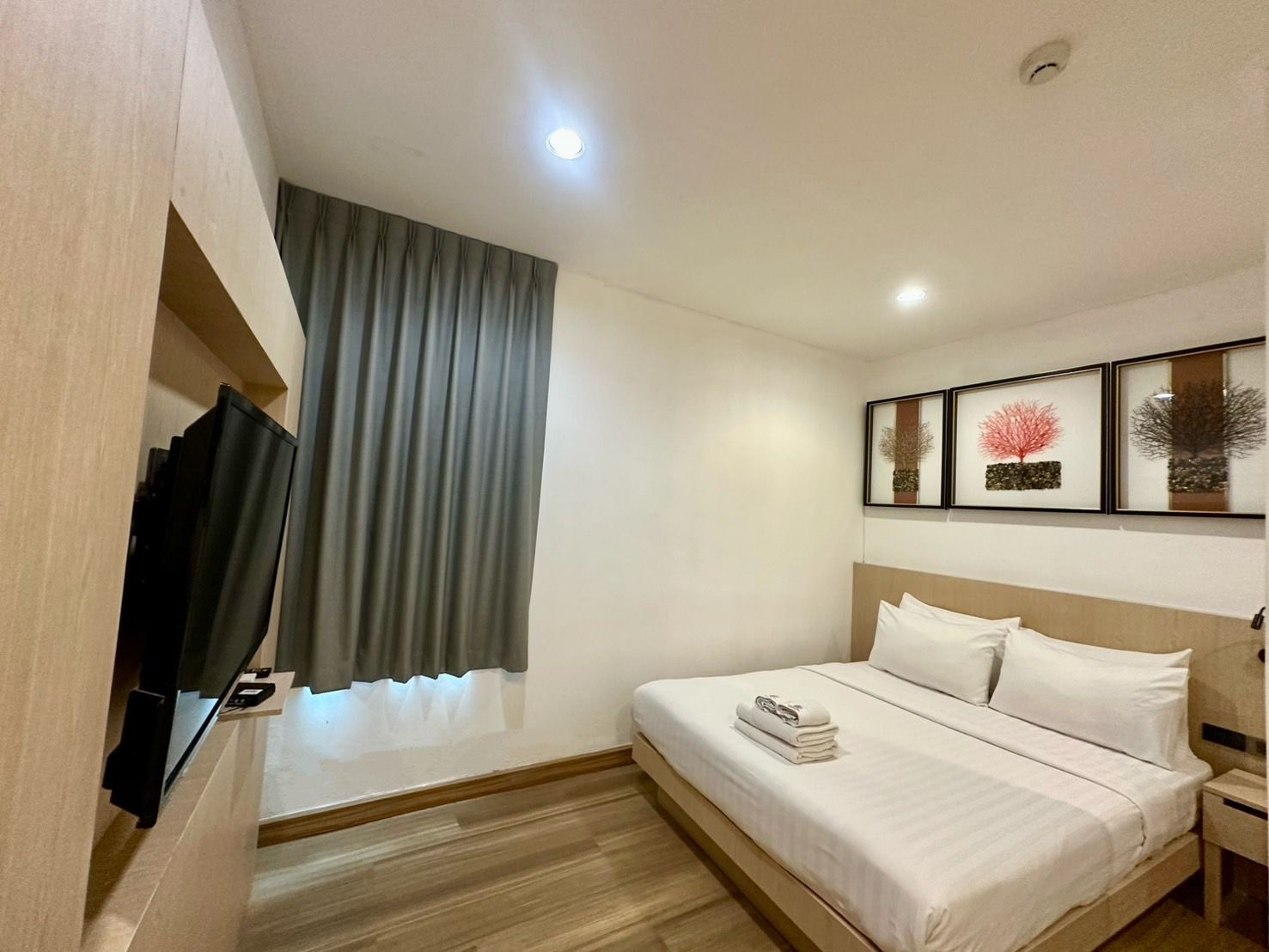 Hotel room with bed, TV, window with gray curtains, and framed wall art.