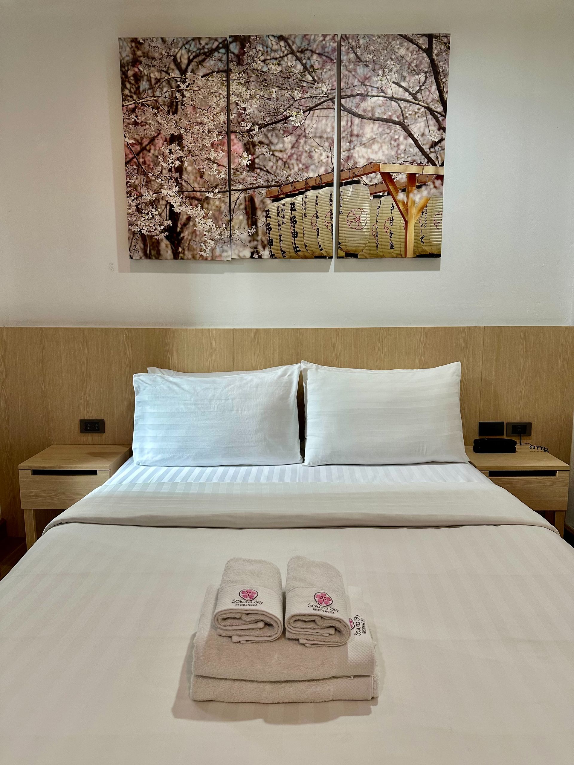 Hotel bedroom with white bedding, towels, and landscape artwork.