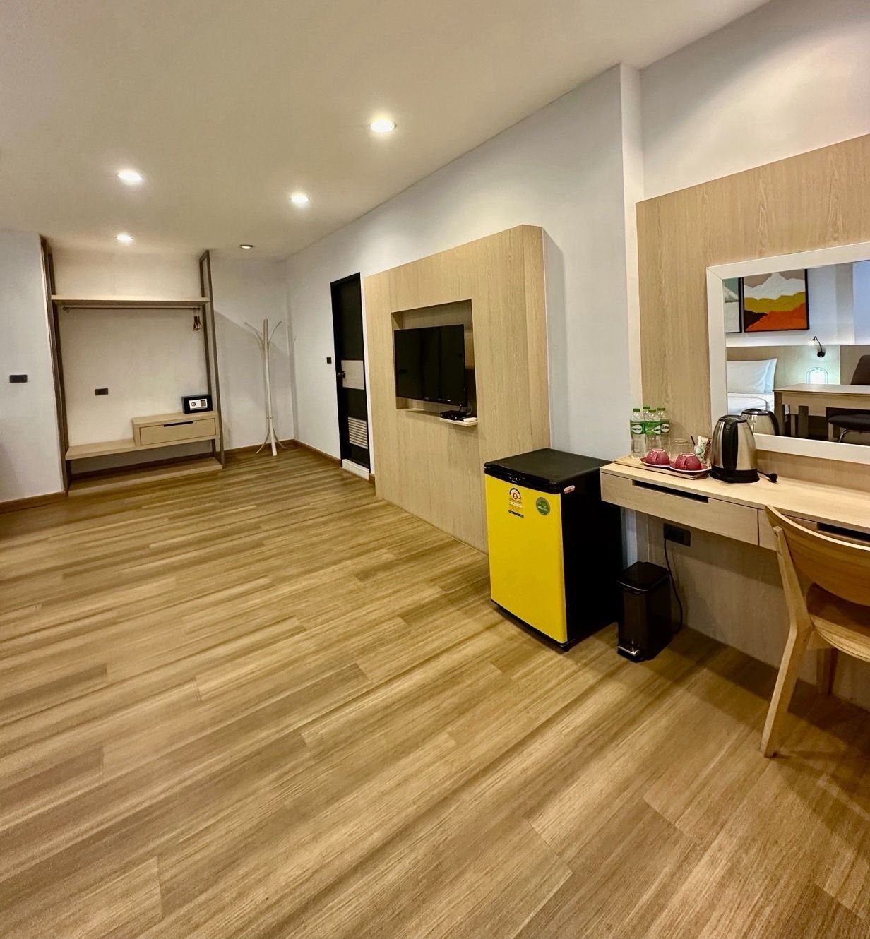 Hotel room interior with wood floors, TV, desk, and yellow mini-fridge.