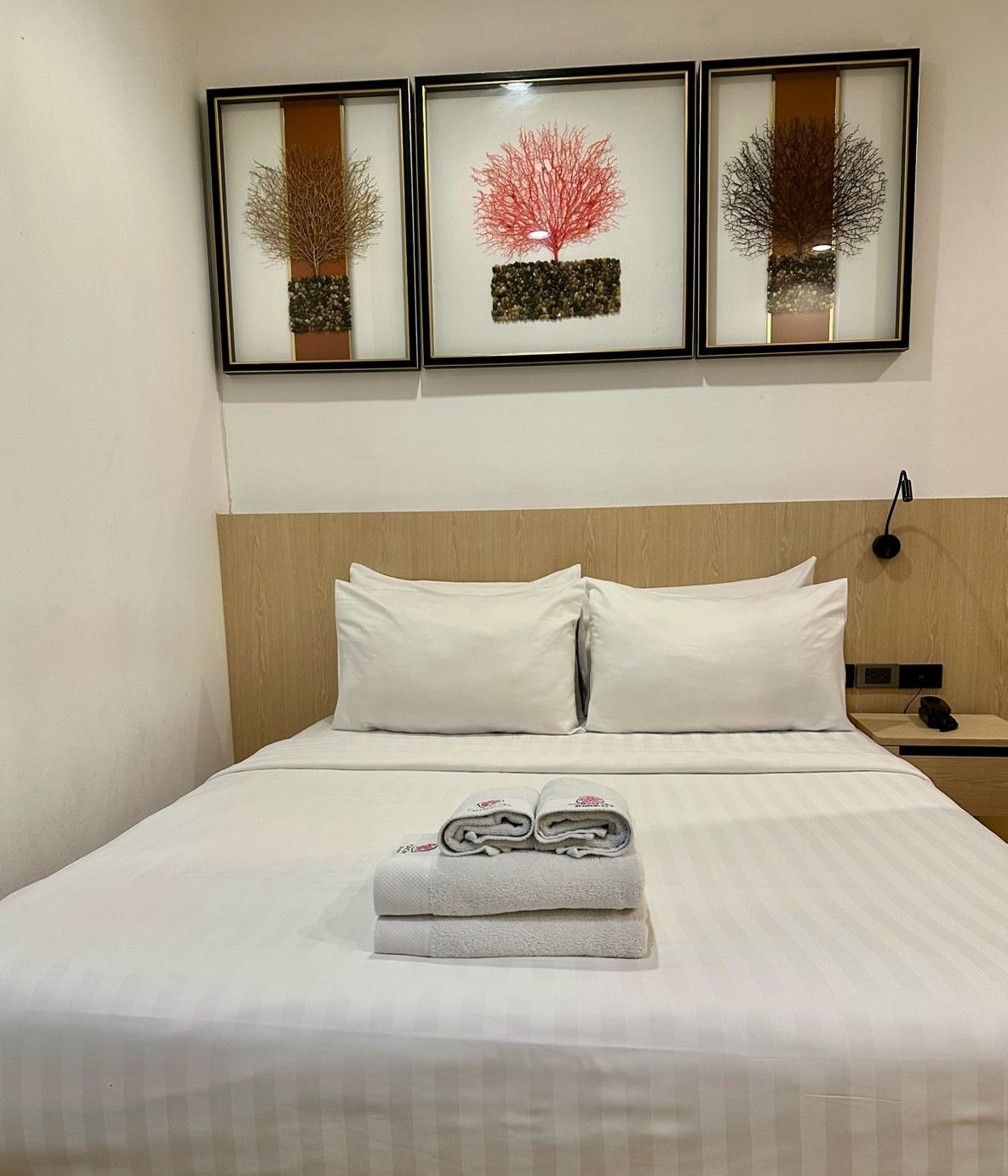 Bedroom with a made bed, white linens, folded towels, and three framed abstract art pieces above the headboard.