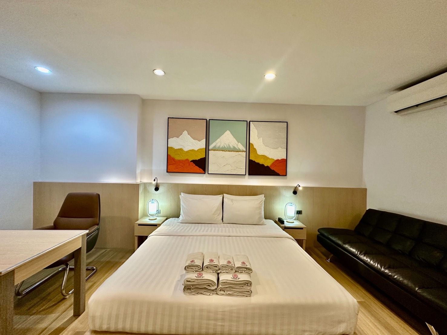 Hotel room with a bed, artwork, a table, a chair, and a black sofa.