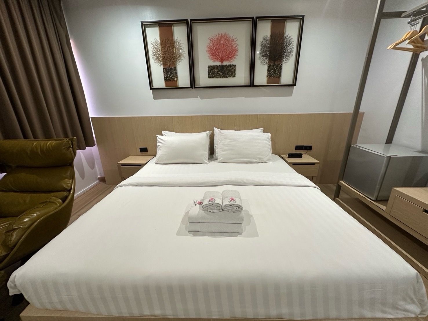 Hotel room with a bed, artwork, a chair, and a mini-fridge.