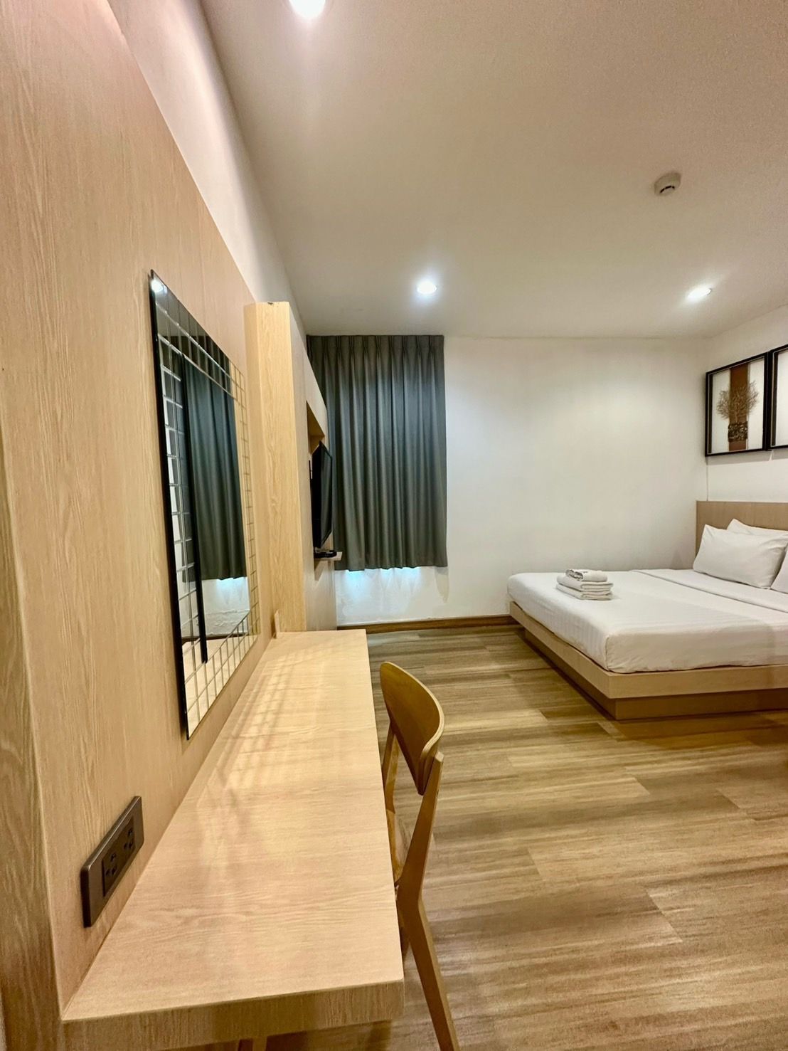 Hotel room with bed, desk, mirror, and window with curtains.