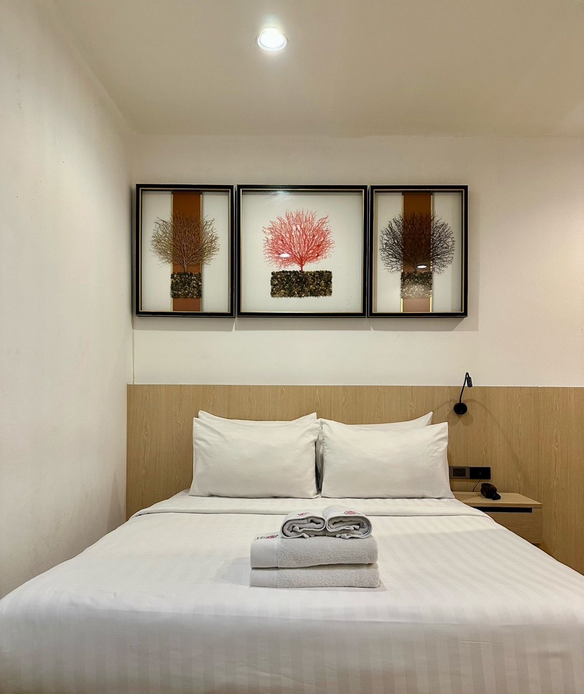 Hotel bed with white linens, three framed art pieces, and a nightstand.