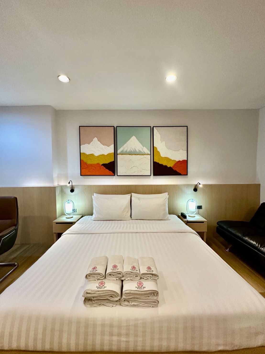 Bedroom with a large bed, three mountain paintings, and folded towels.