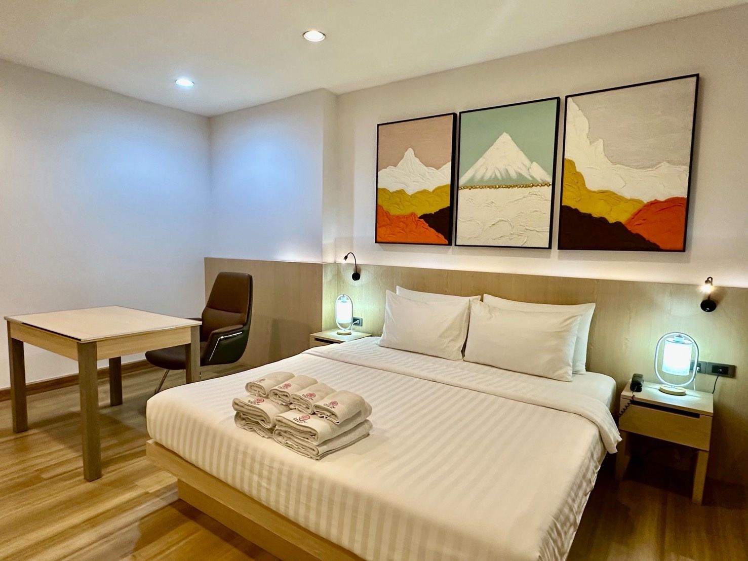 Bedroom with a double bed, bedside tables, and abstract mountain art. A desk and chair are on the left.