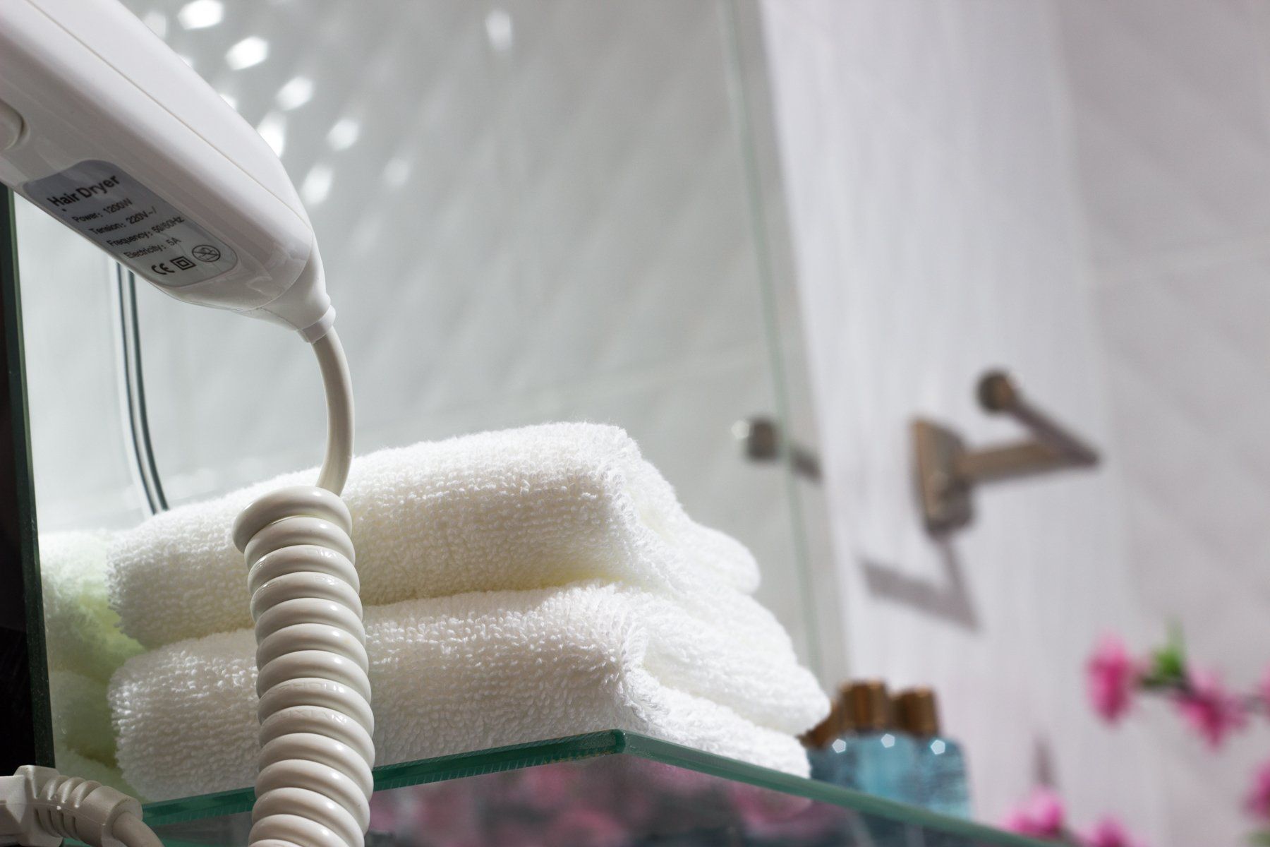 White towels stacked on a glass shelf in a bathroom with a hairdryer.