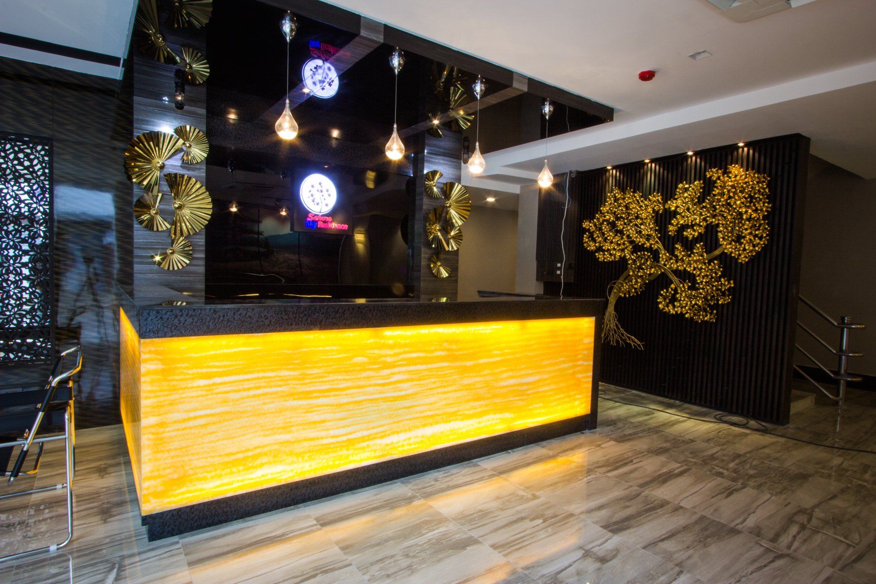 Reception desk with gold lighting, marble floor, and decorative wall art.