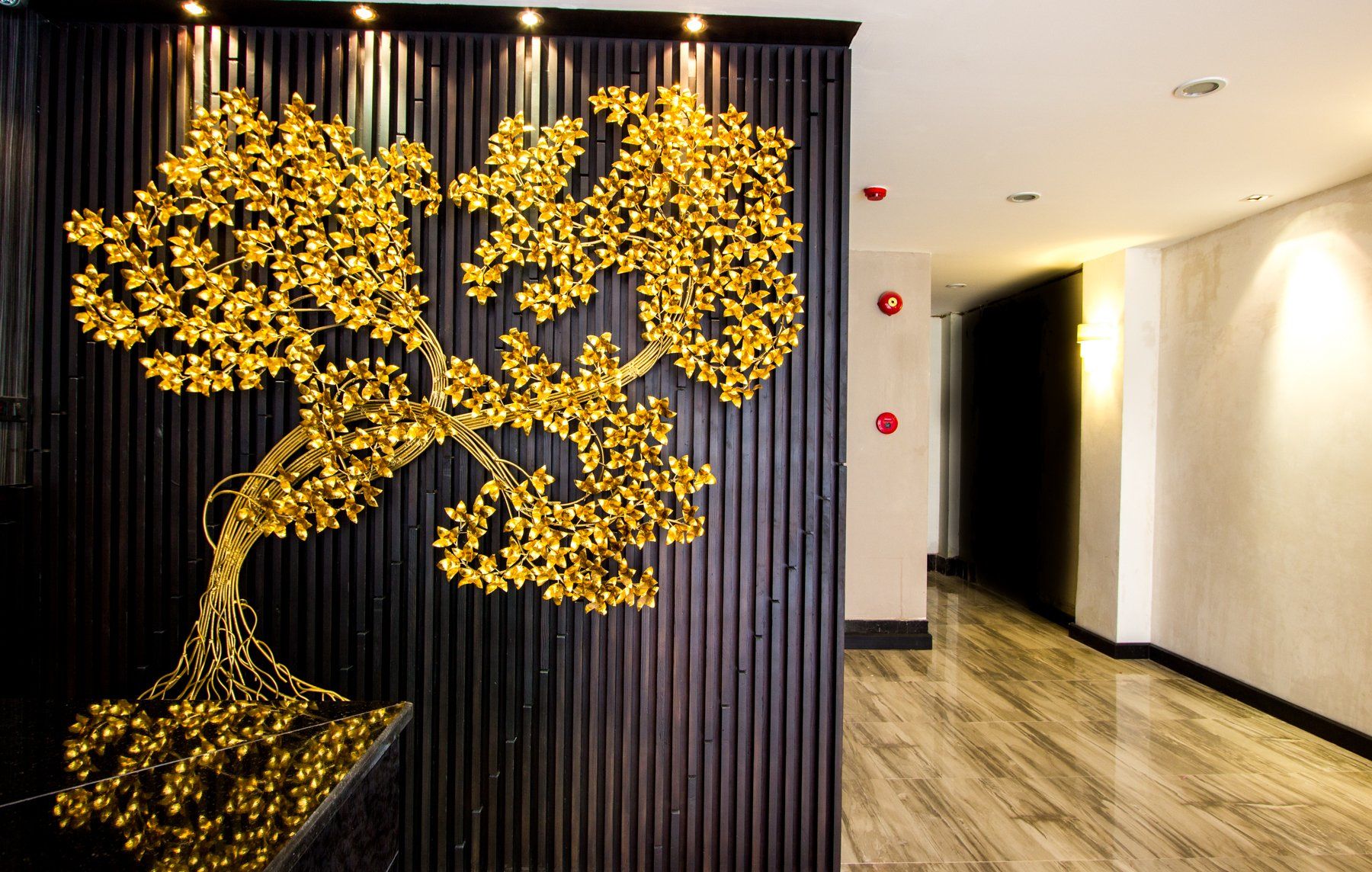 Gold tree sculpture on a dark, textured wall in a hallway with a marble floor.