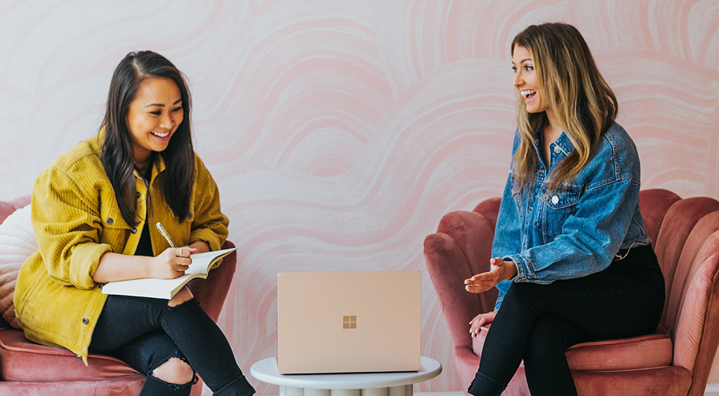 Two women are sitting in chairs with a laptop on a table.
