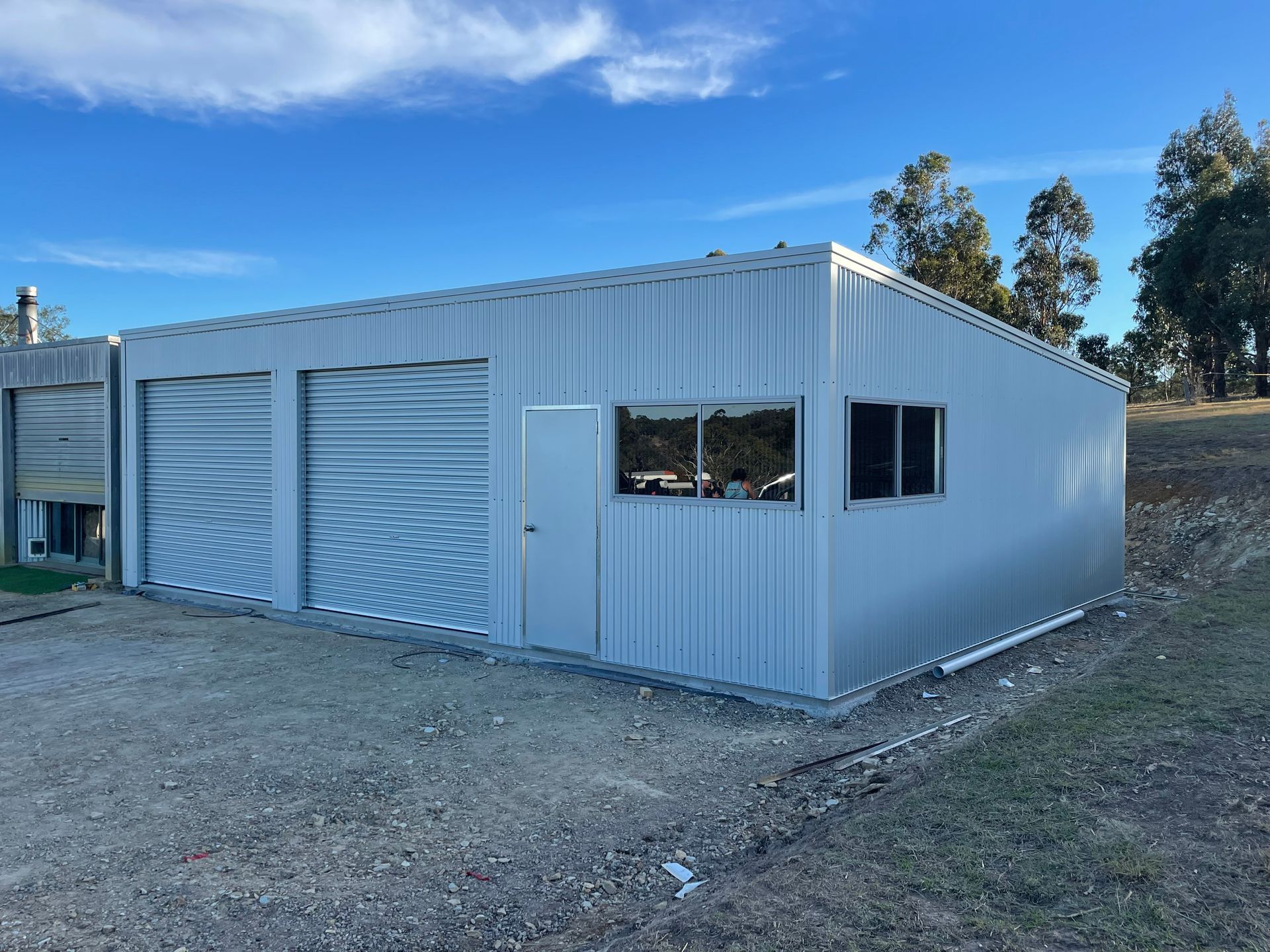 White metal storage building with large roll-up doors on a gravel lot under a blue sky