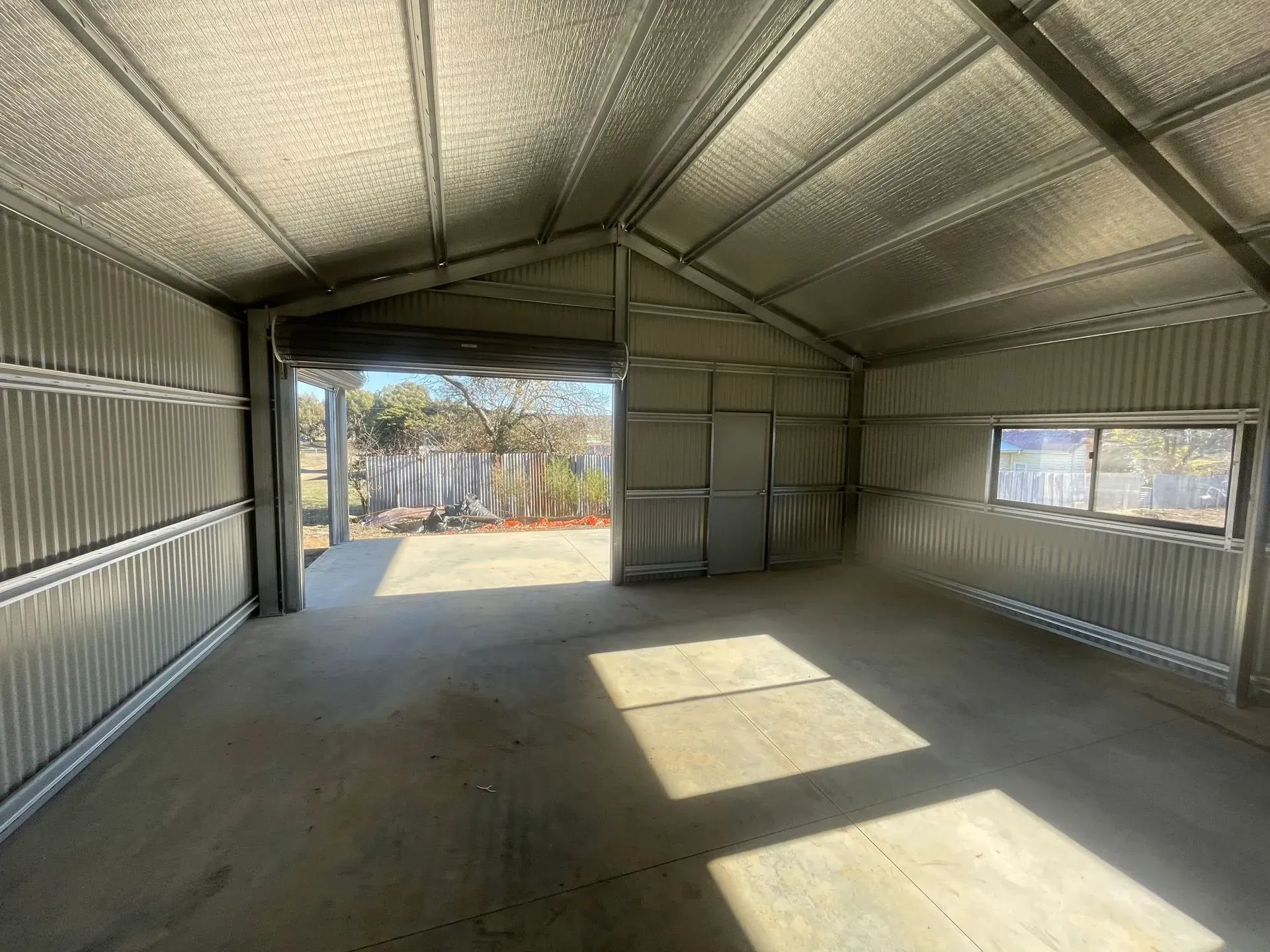 Empty metal shed interior with open doorway and bright sunlight on the floor