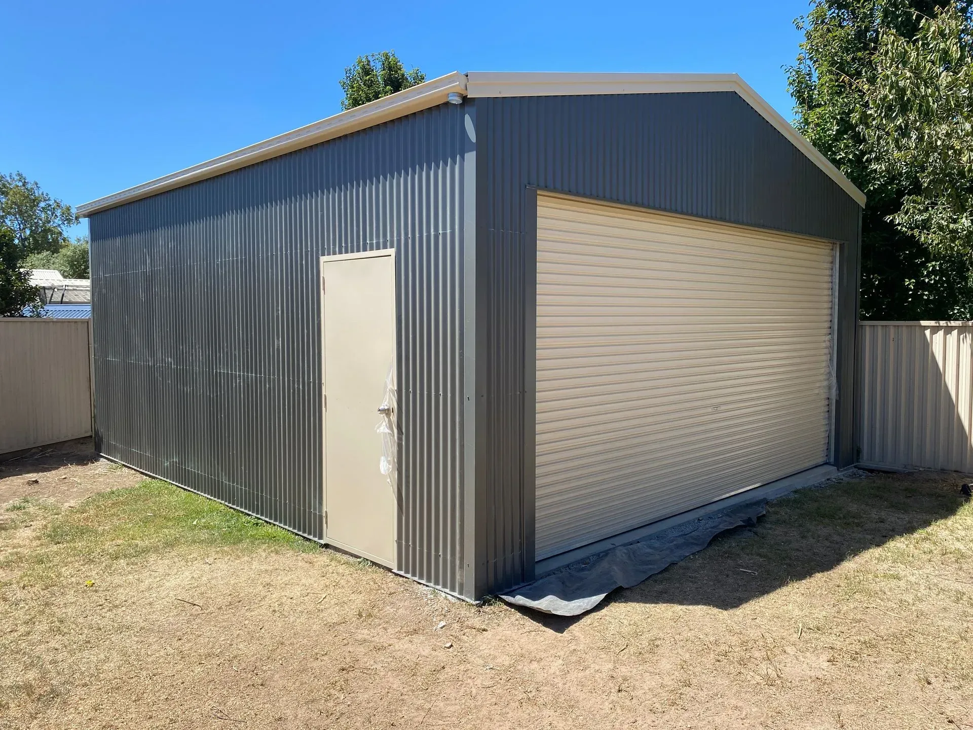 Gray metal garage shed with a roll-up door and side entry door on a dirt lot