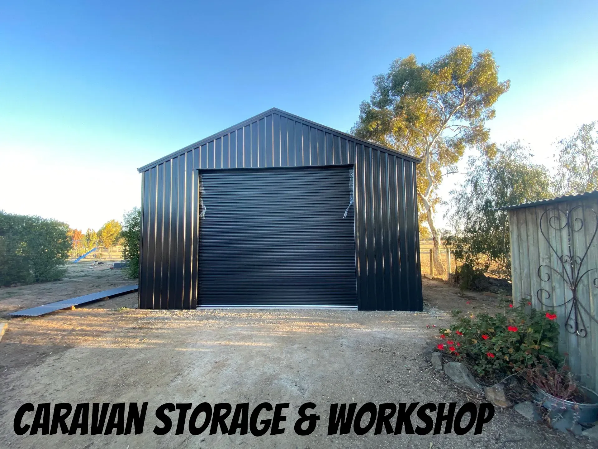 Black metal caravan storage and workshop building with a large roller door in a rural setting