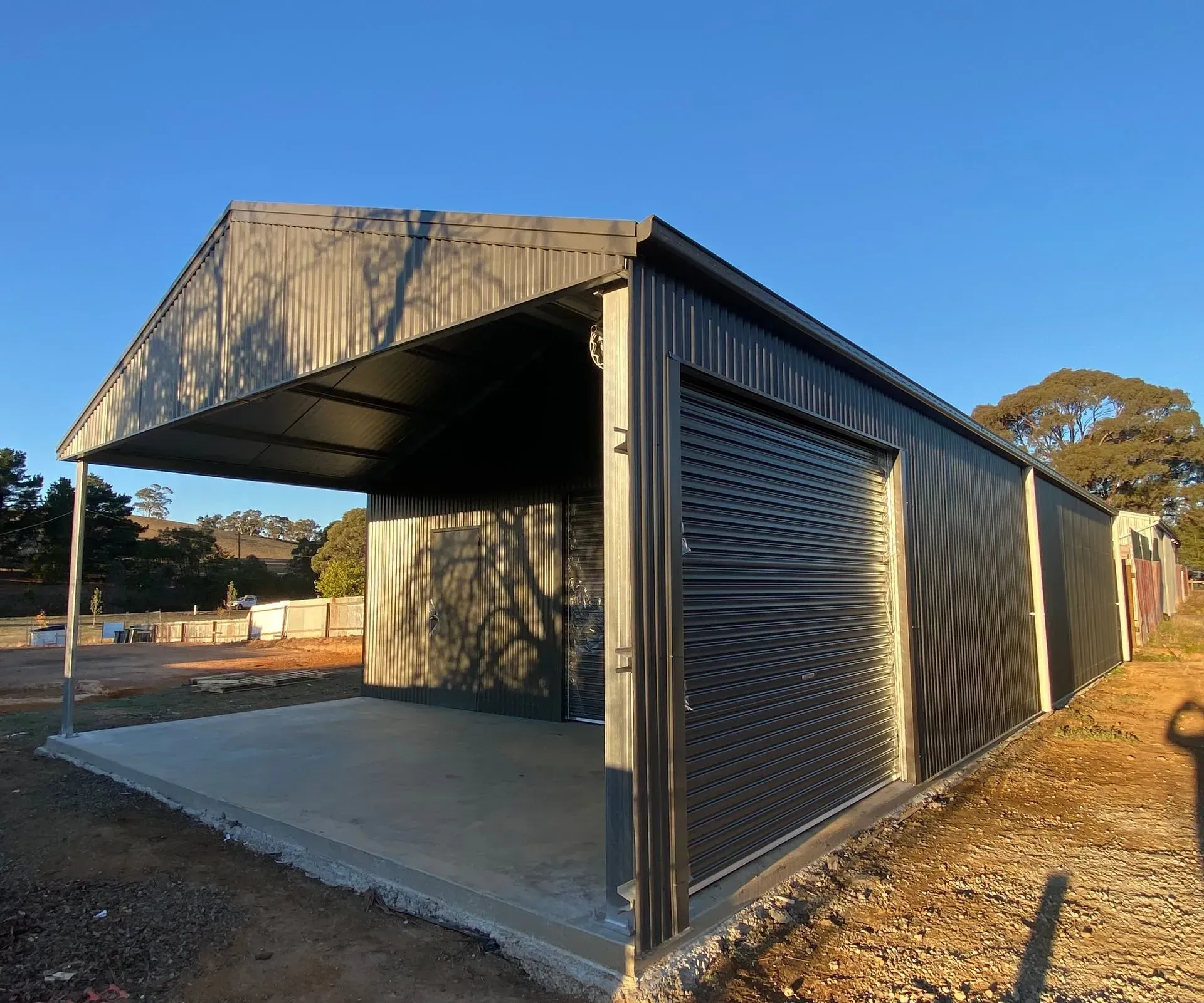 Modern black metal building with a large covered opening, shown outdoors on a dirt lot.