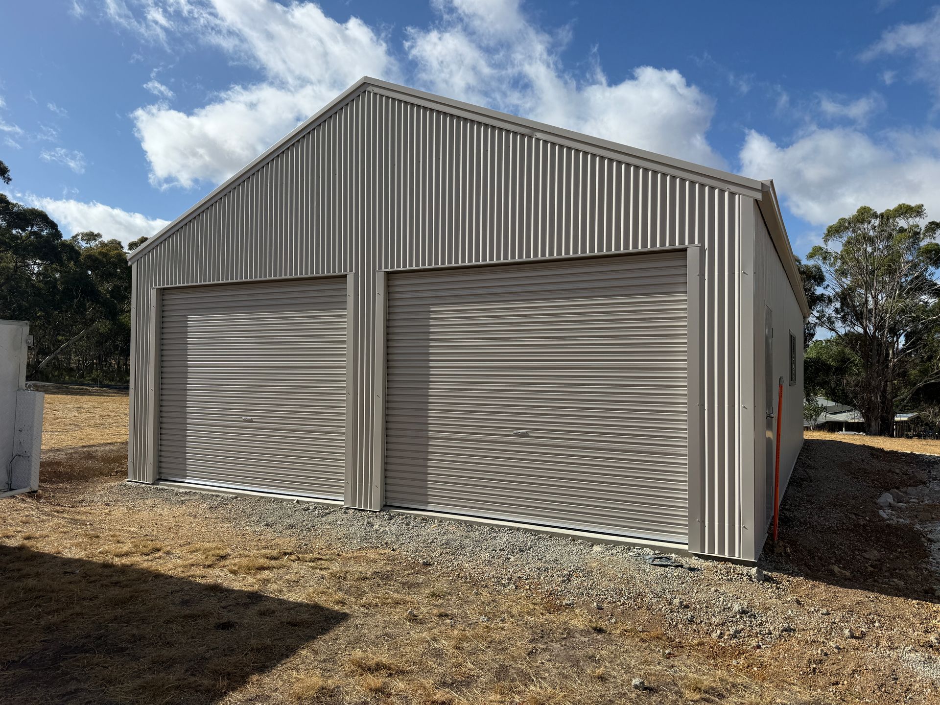 Metal storage shed with two roll-up doors on a gravel lot under a partly cloudy sky