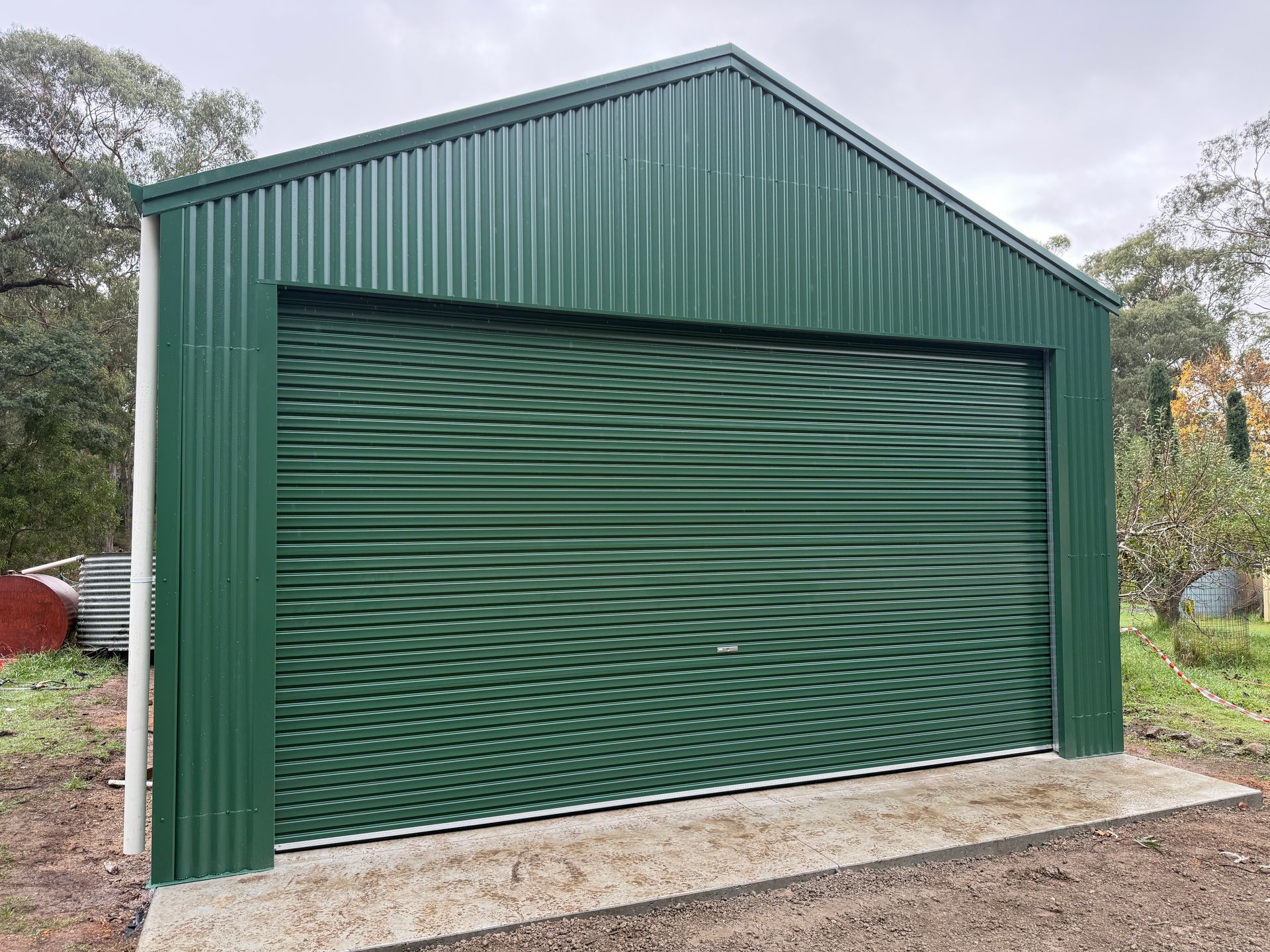 Green metal shed with a large roll-up door on a concrete slab outdoors