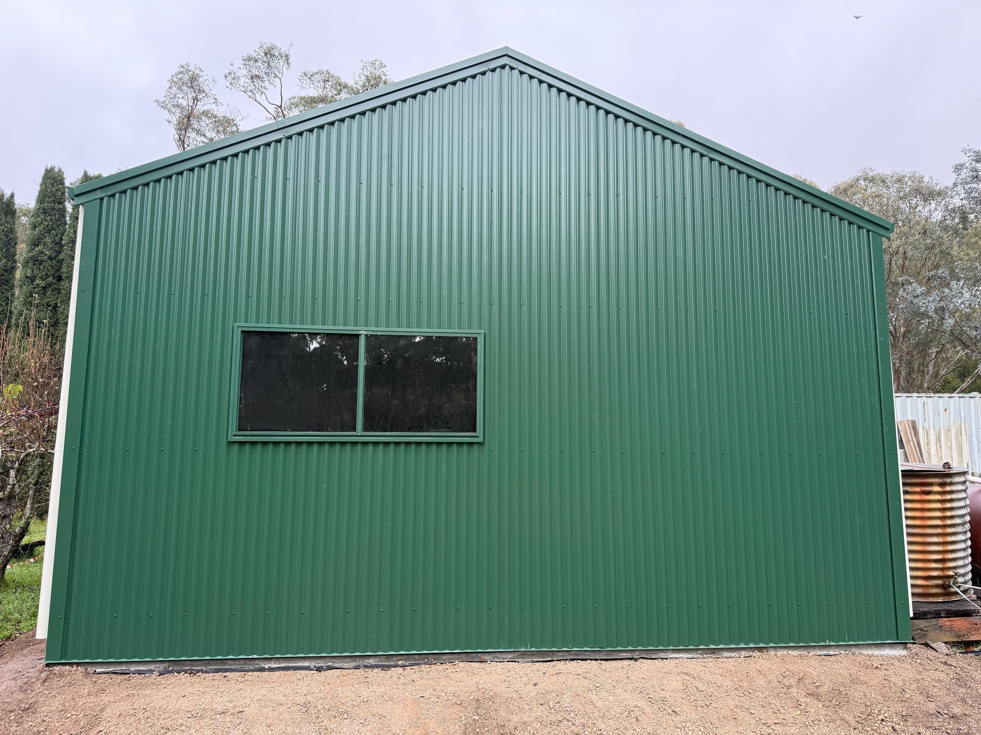 Green metal building with a sloped roof and a small window on the front.