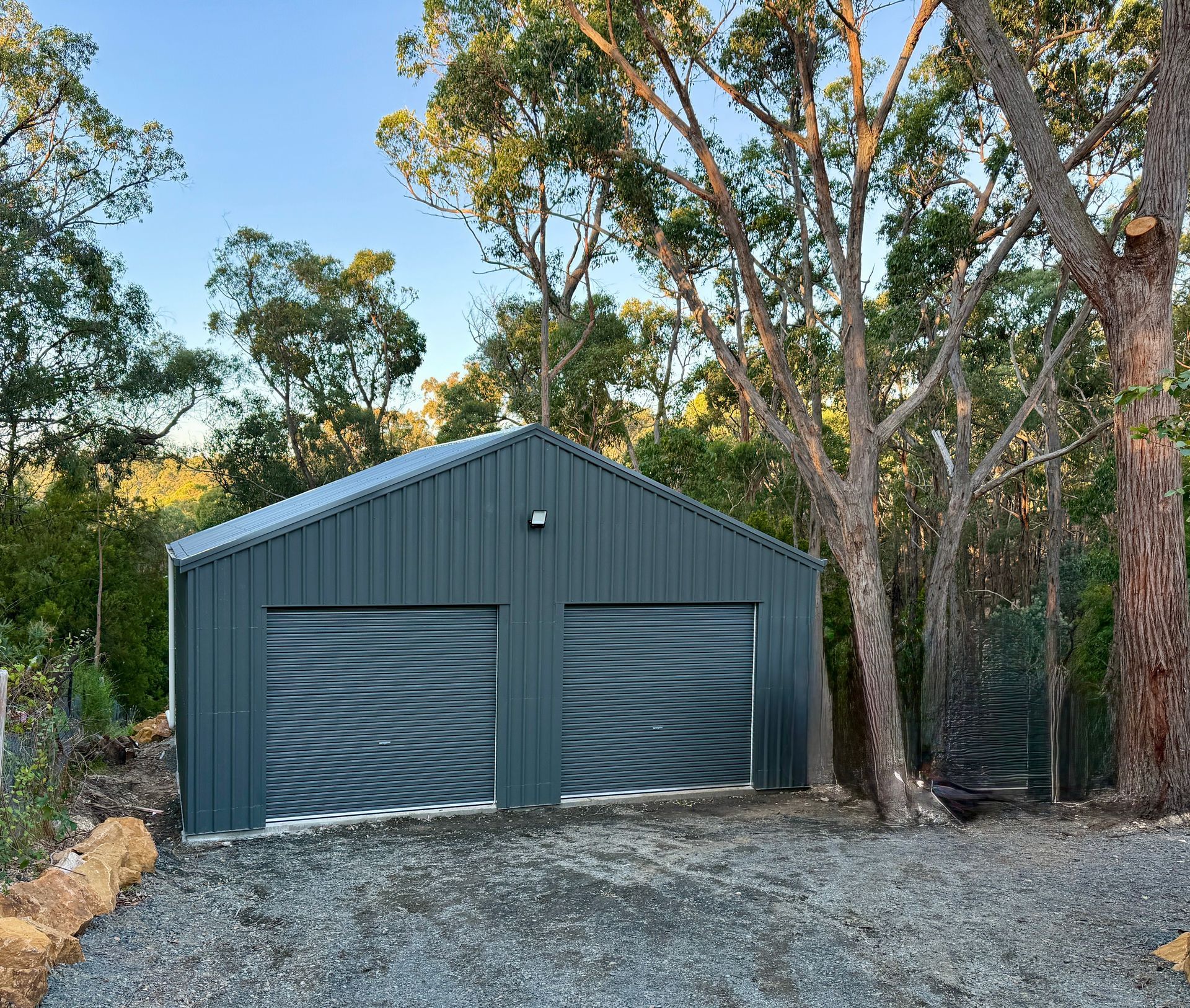 Gray double garage with corrugated doors beside trees on a gravel driveway.