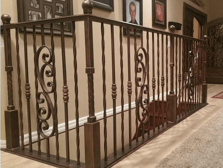 Brown wrought-iron stair railing with decorative scrollwork, installed on a beige wall in a home interior.