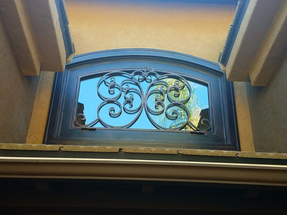 Ornate wrought-iron window with a decorative scrollwork pattern, set in an exterior wall.