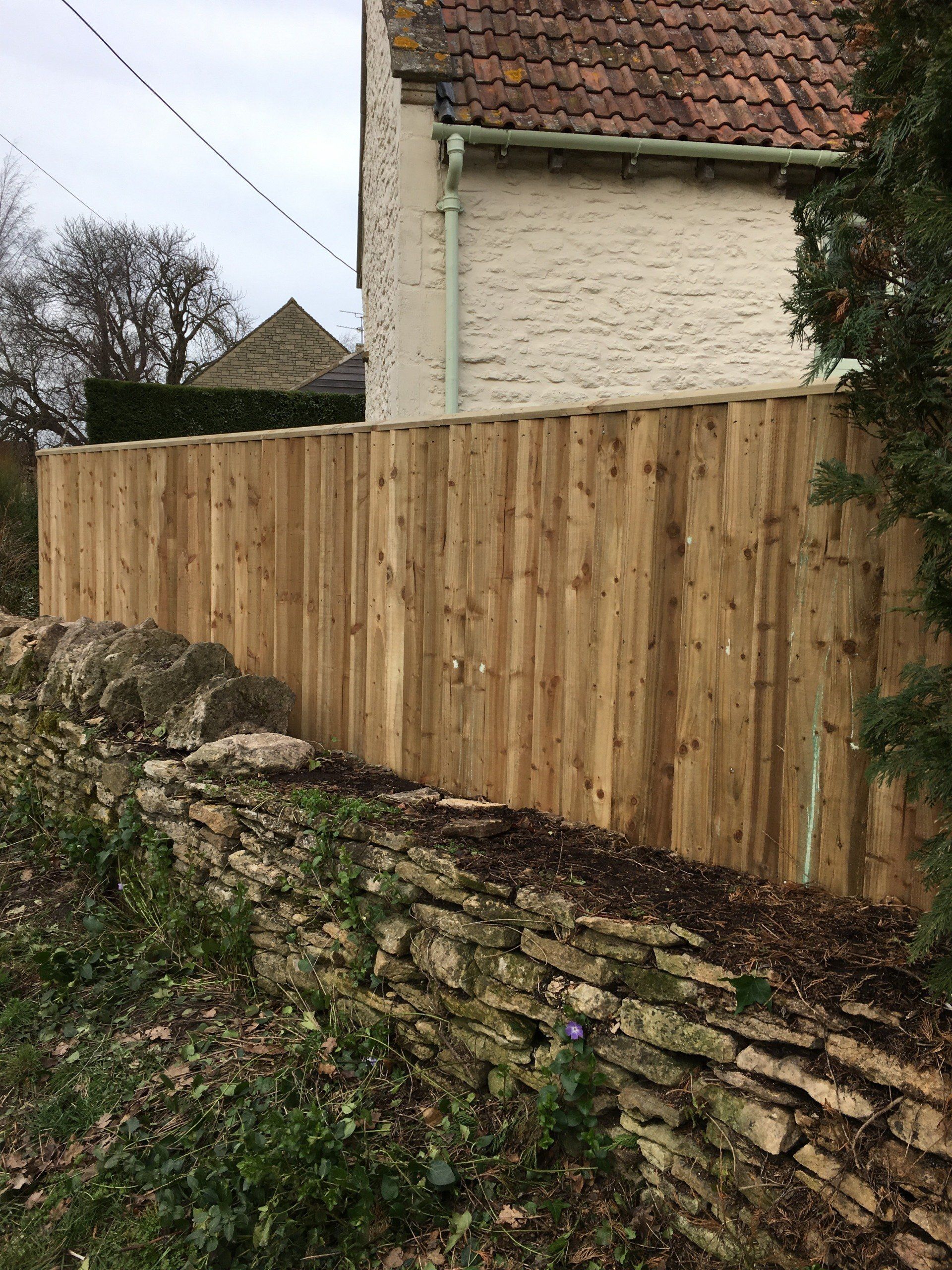 A wooden fence surrounds a stone wall next to a house.