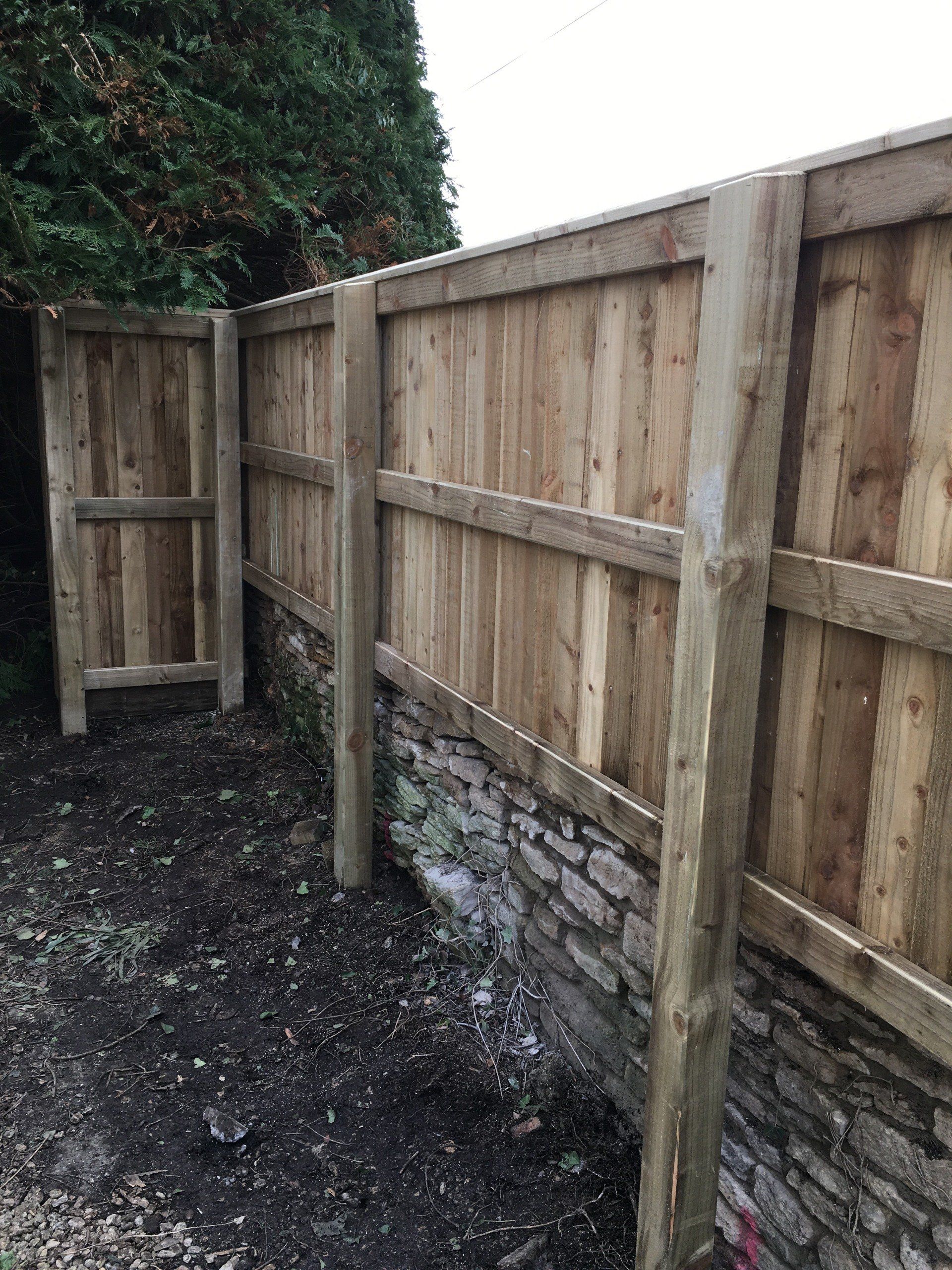 A wooden fence is sitting next to a stone wall.