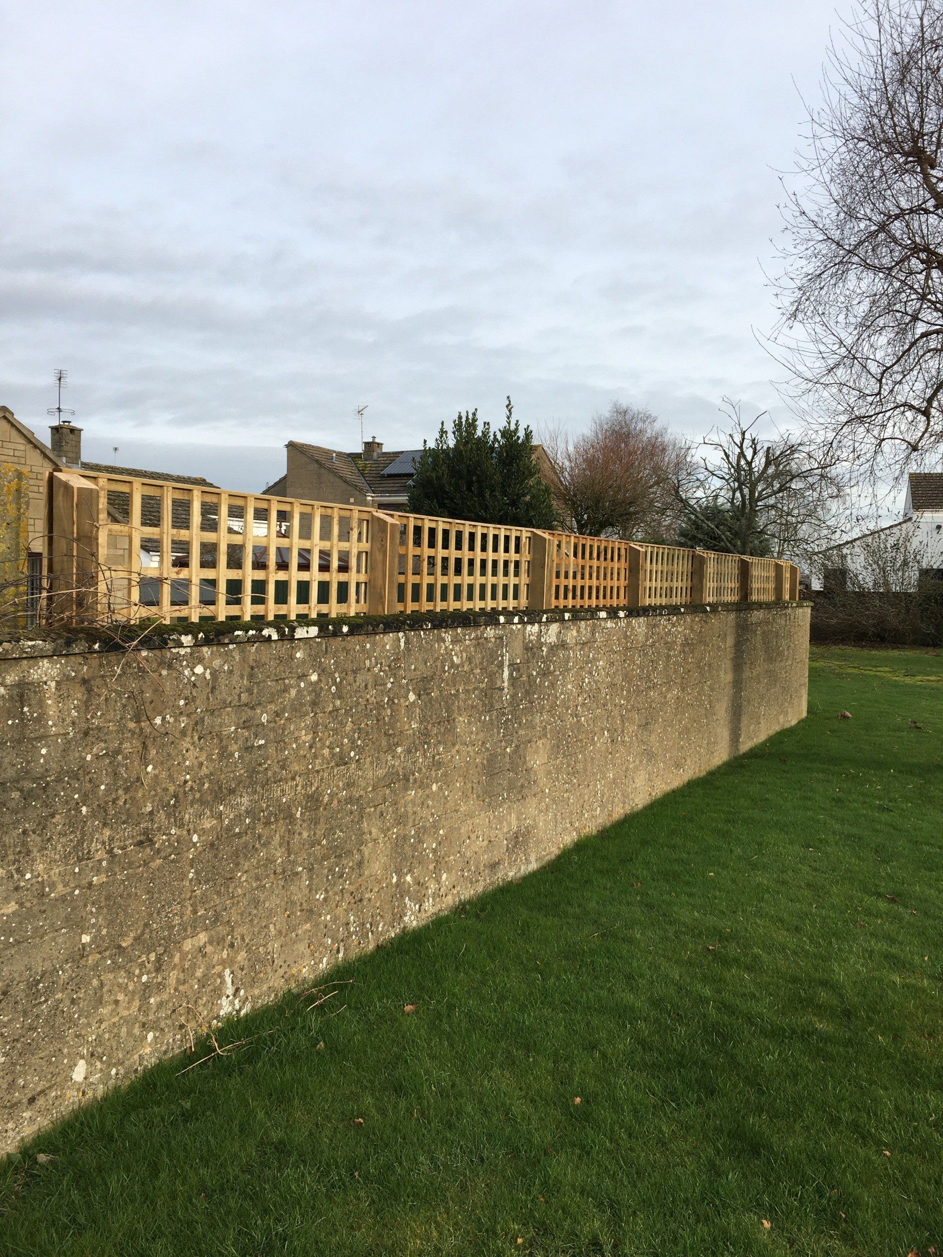 A wooden fence is sitting on top of a stone wall next to a lush green field.