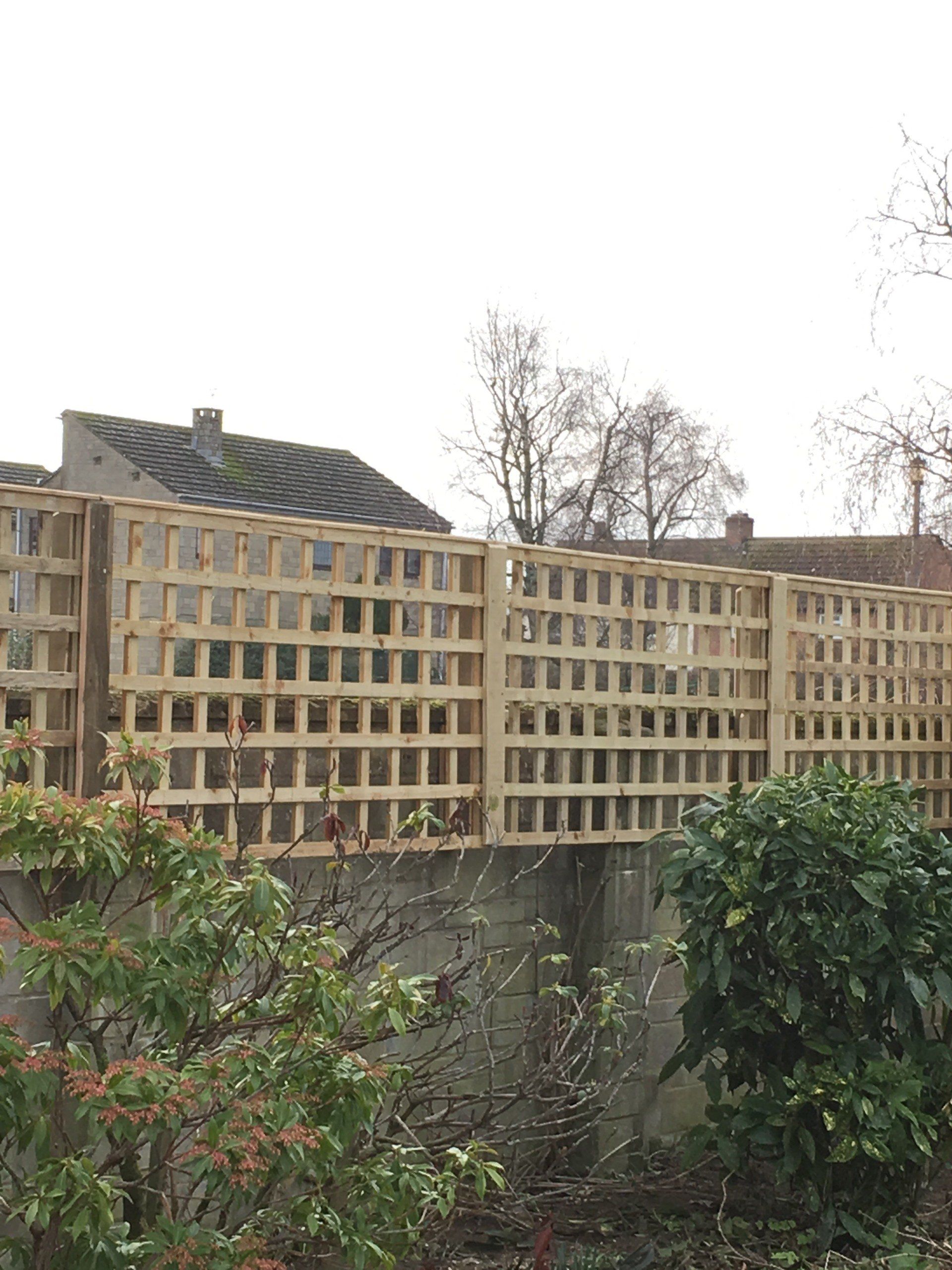 A wooden fence is surrounded by trees and bushes in front of a house.