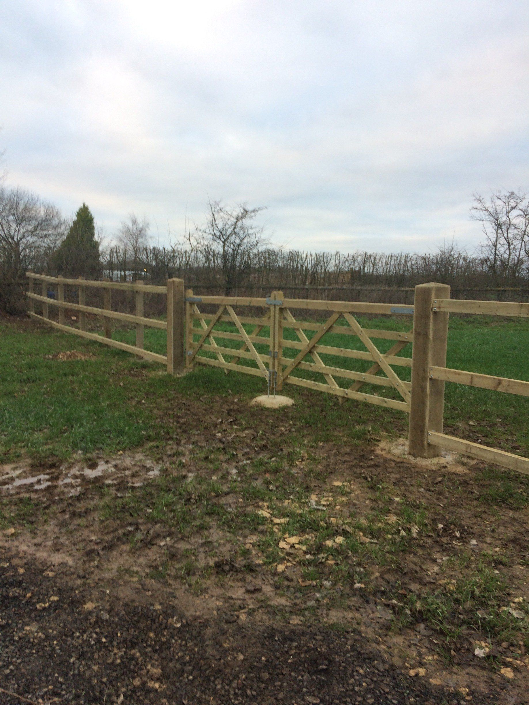 A wooden fence with a gate in the middle of a field.