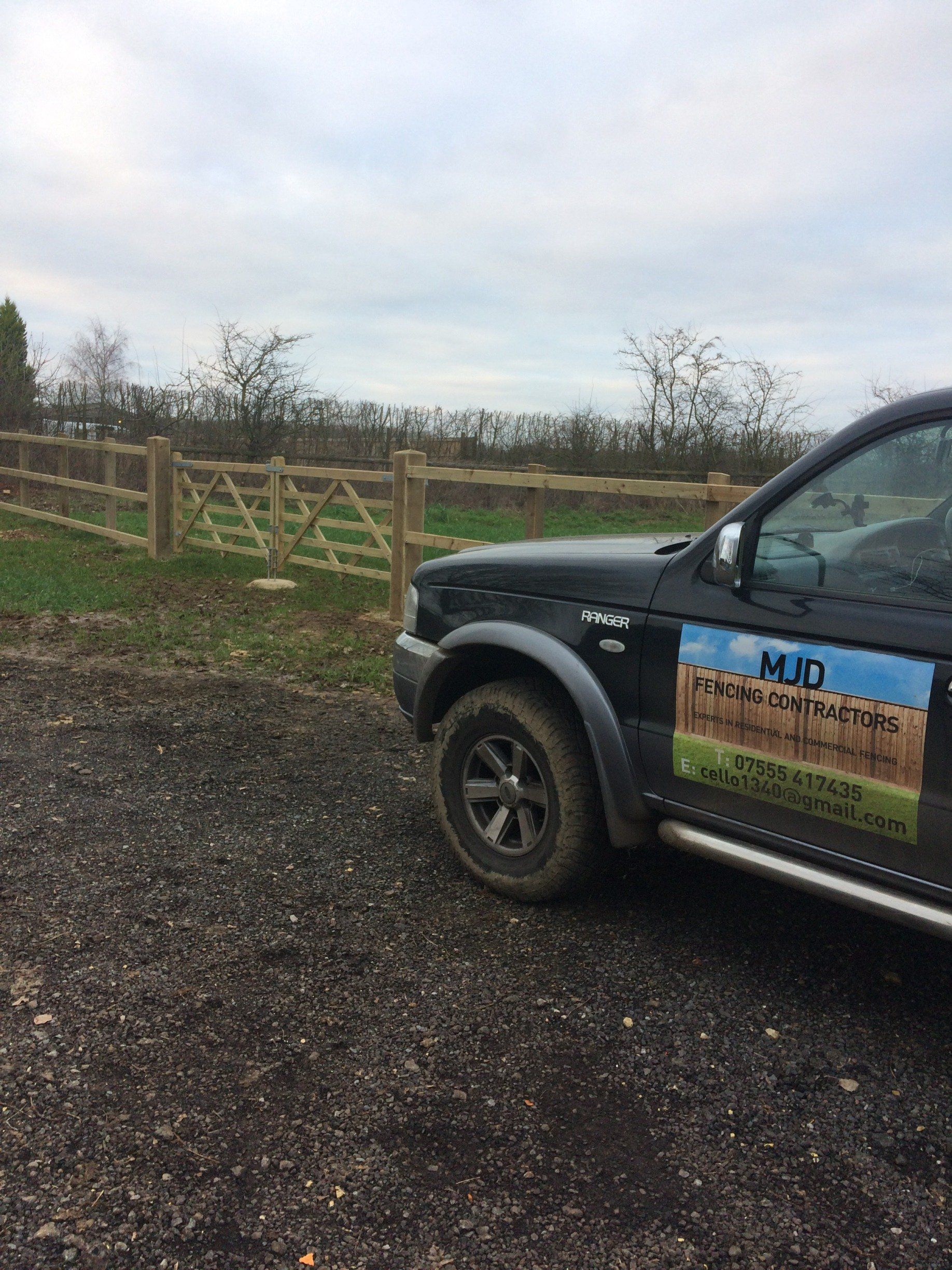 A black truck is parked in a gravel lot next to a wooden fence.