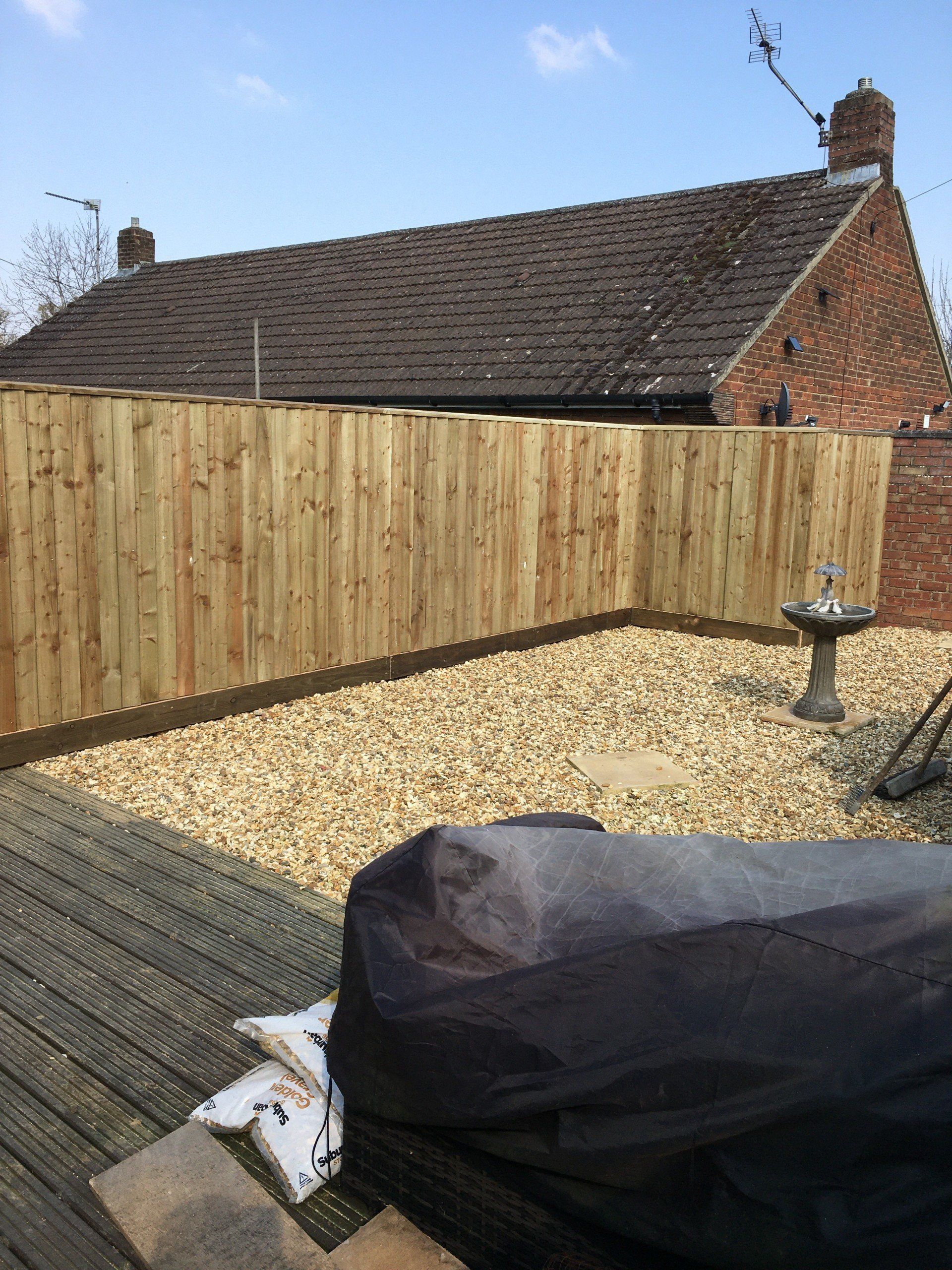 A wooden fence is surrounding a gravel area in front of a house.