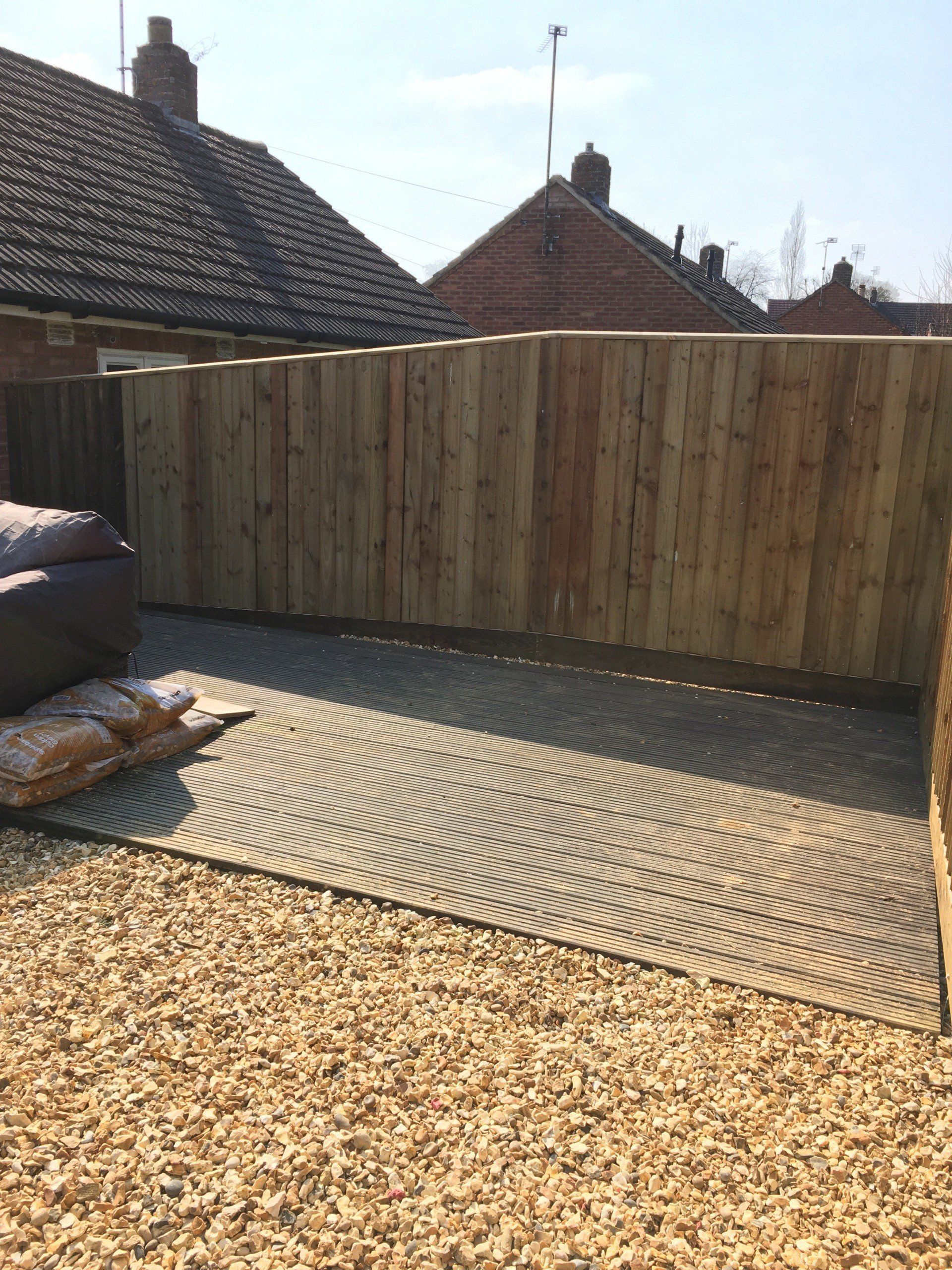 A wooden fence is surrounding a gravel area in a backyard.