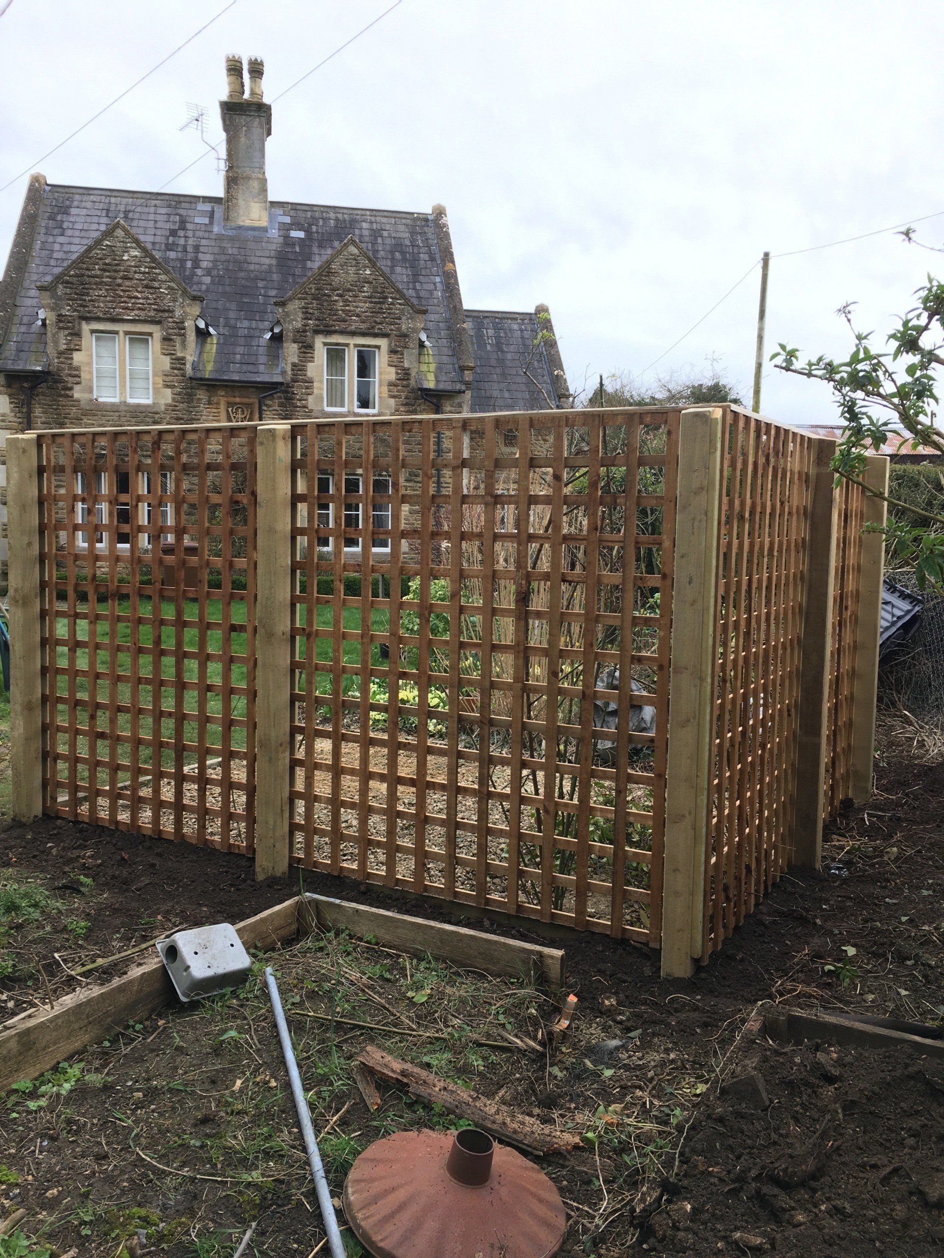 A wooden fence in a garden with a house in the background.