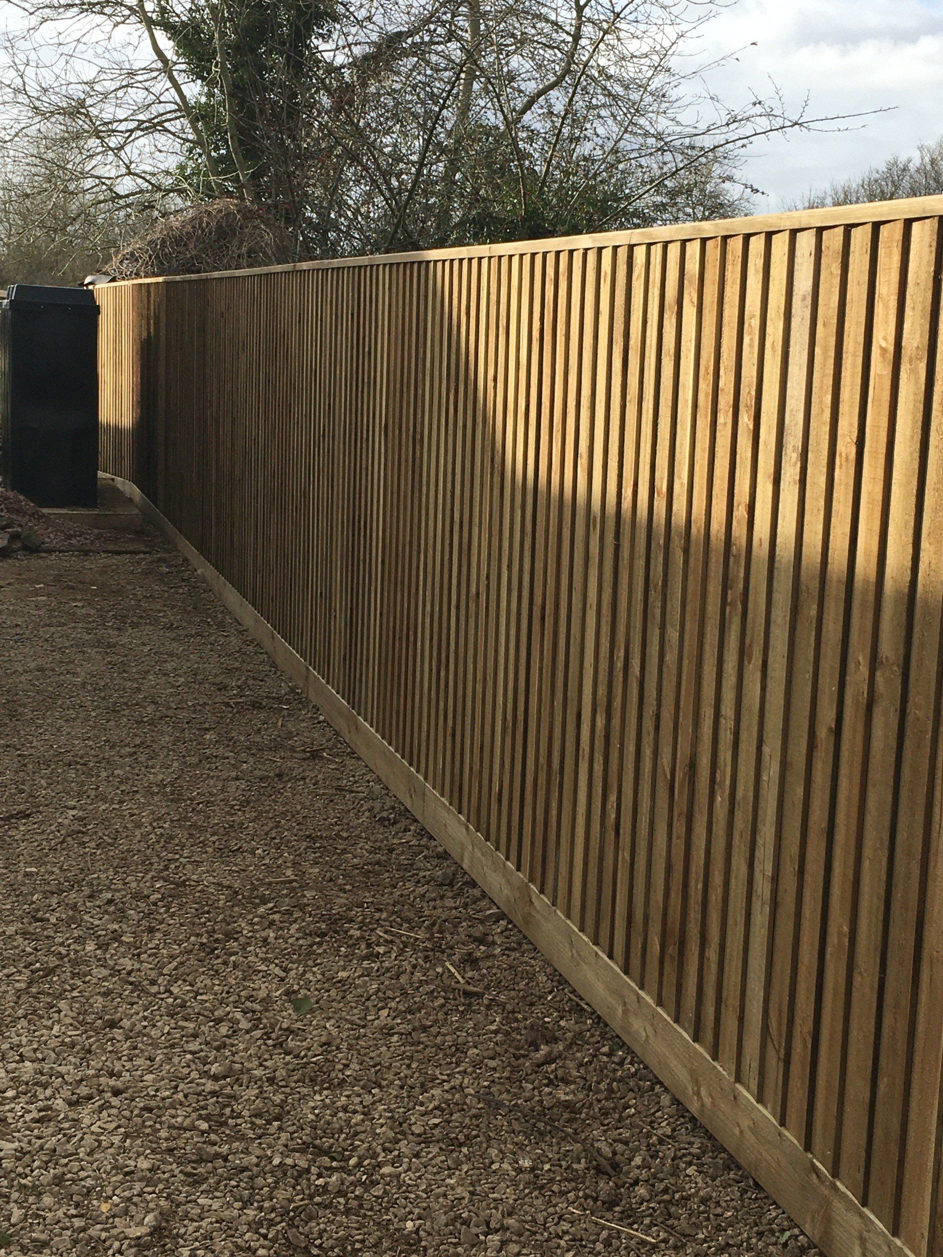 A wooden fence surrounds a gravel area in a backyard.