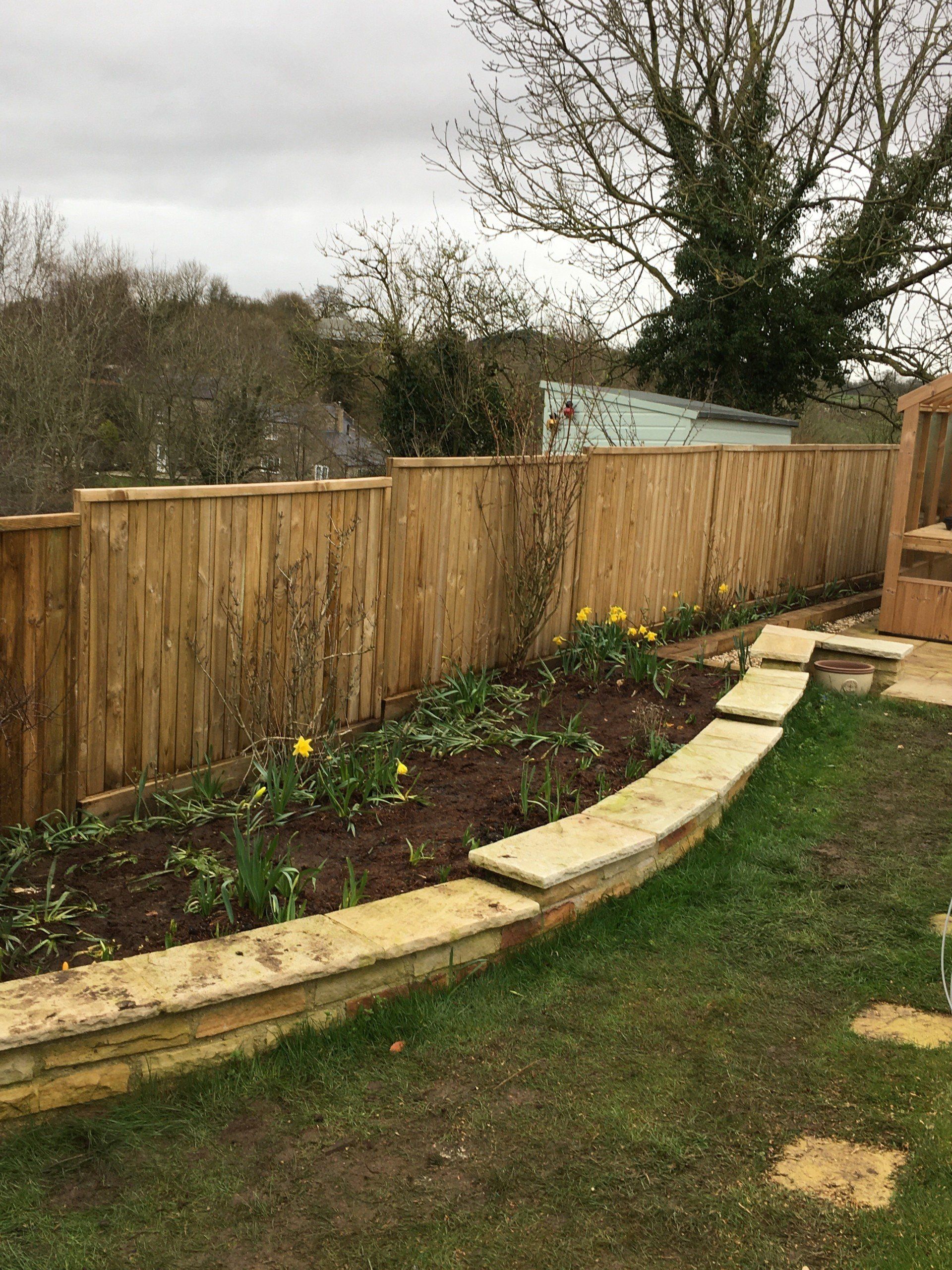 A wooden fence surrounds a garden in a backyard.