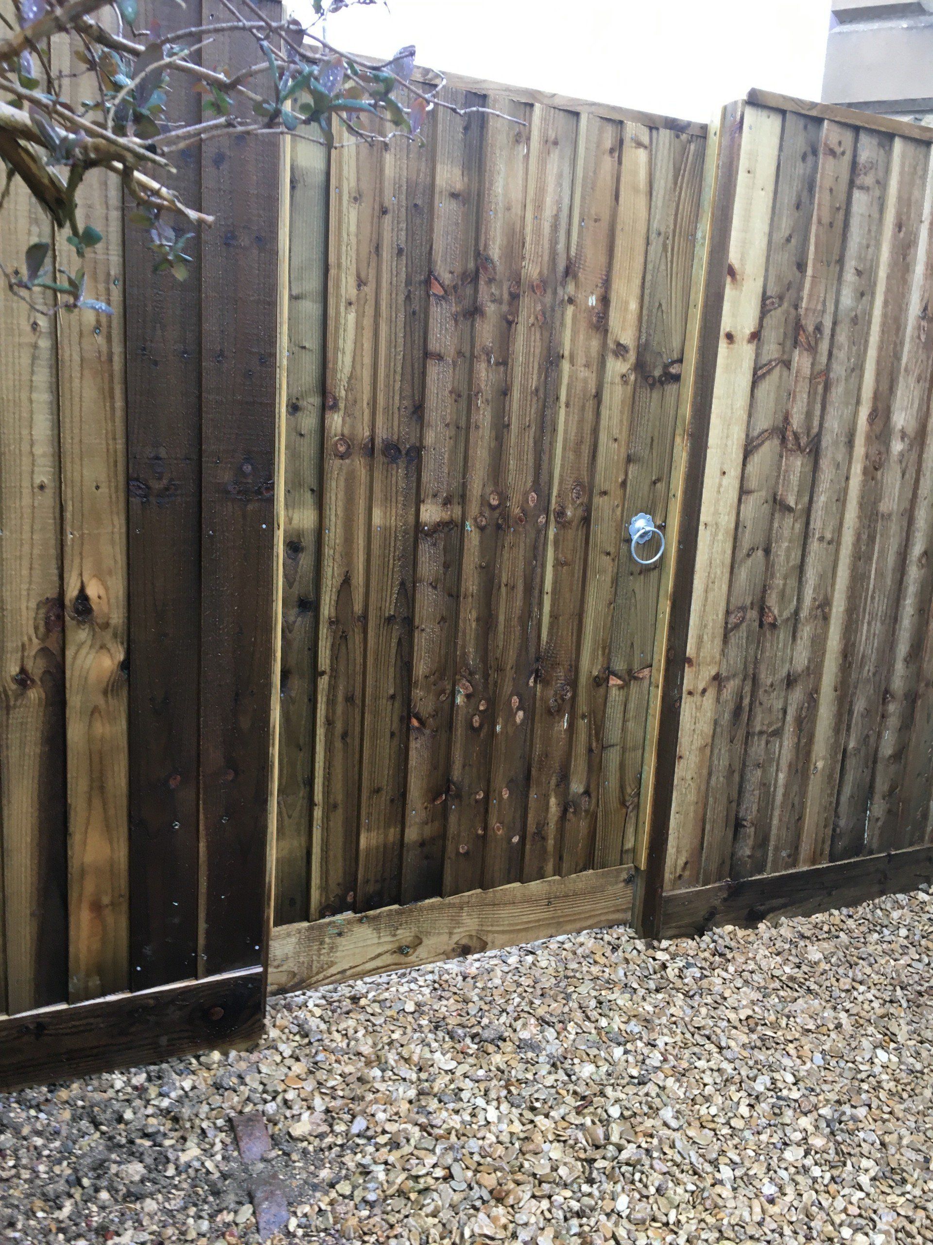A wooden fence with a gate leading to a gravel area.