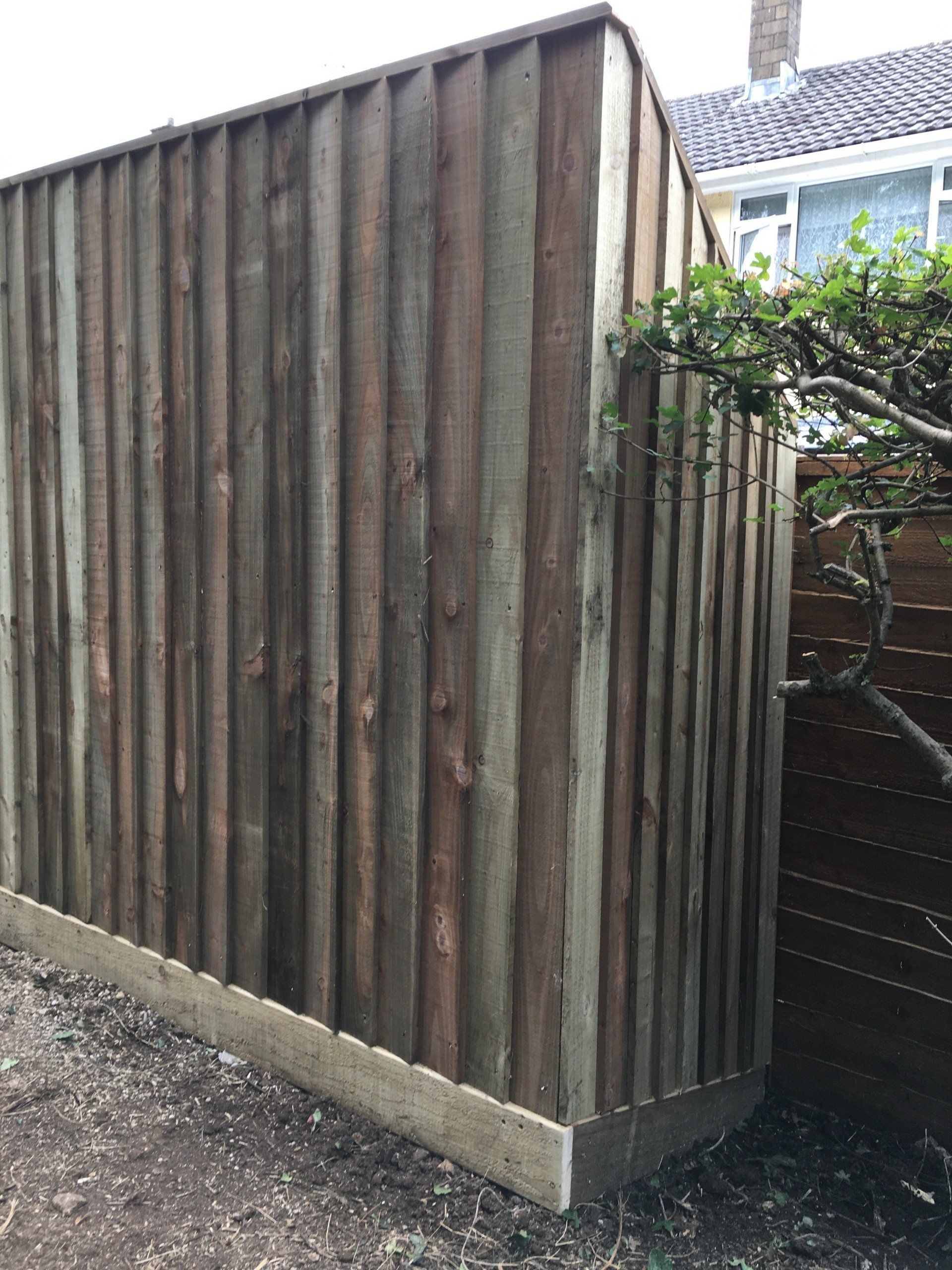 A wooden fence is sitting next to a tree in front of a house.