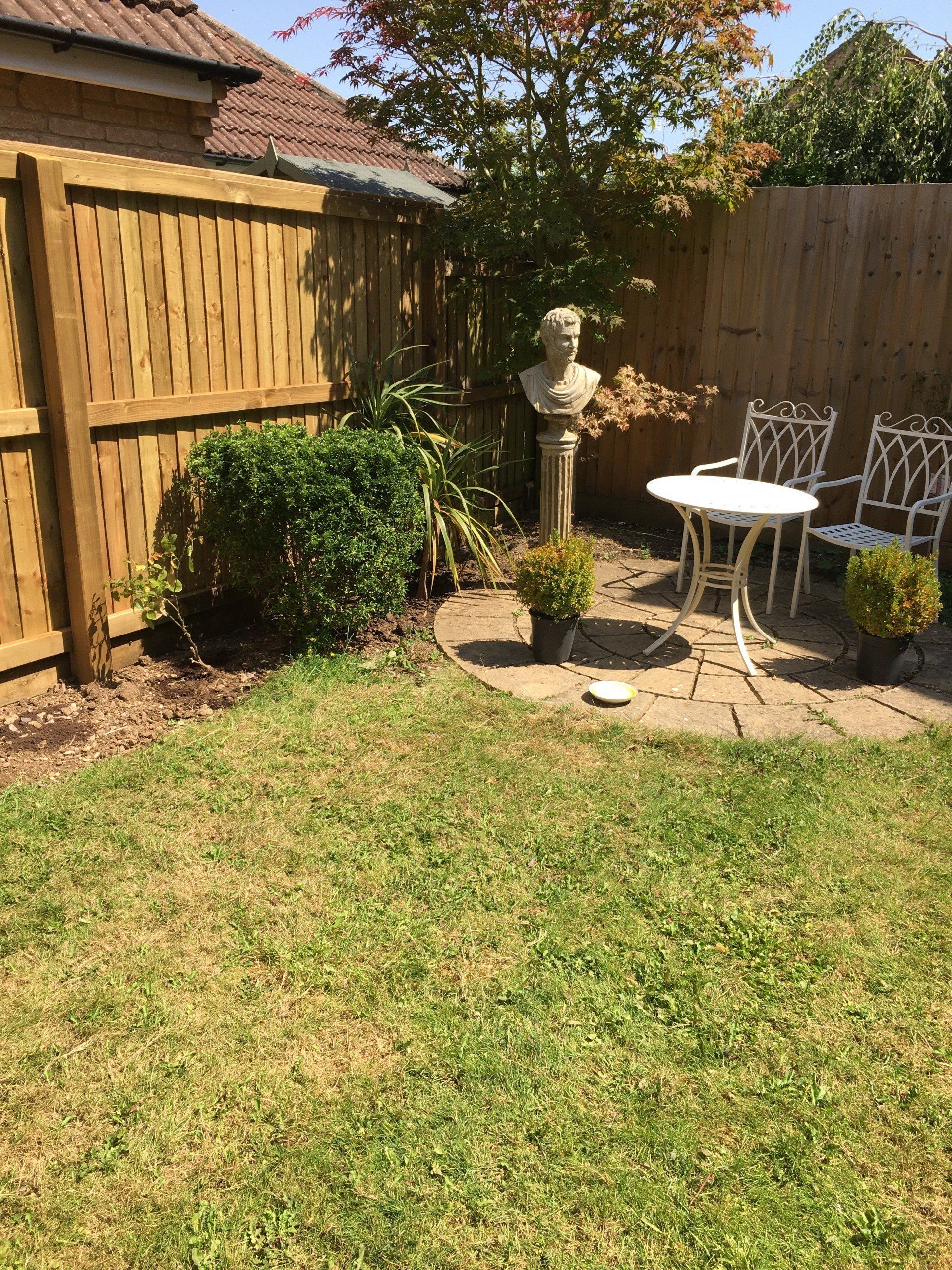 A garden with a wooden fence , chairs , a table and a statue.