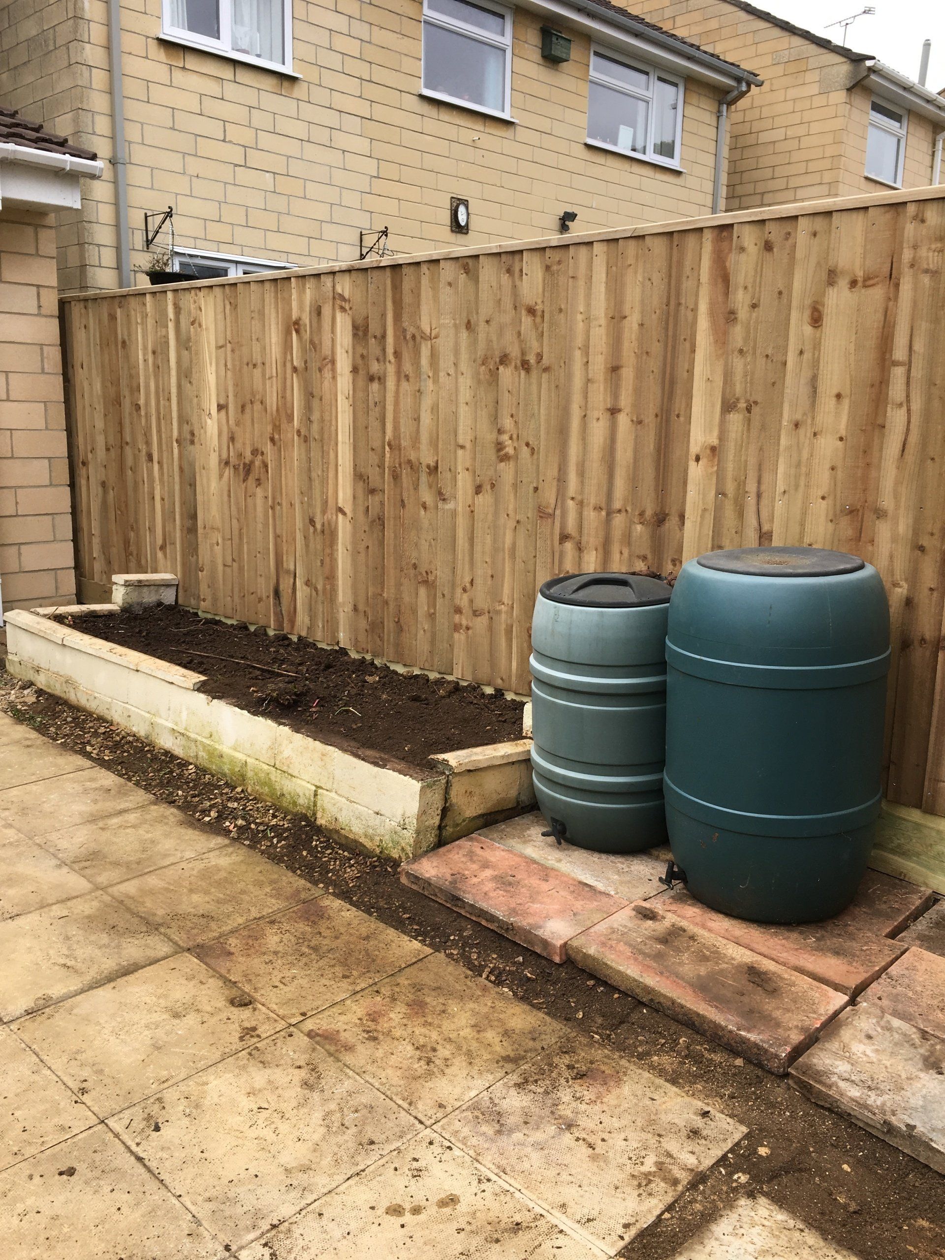 Two green barrels are sitting next to a wooden fence.