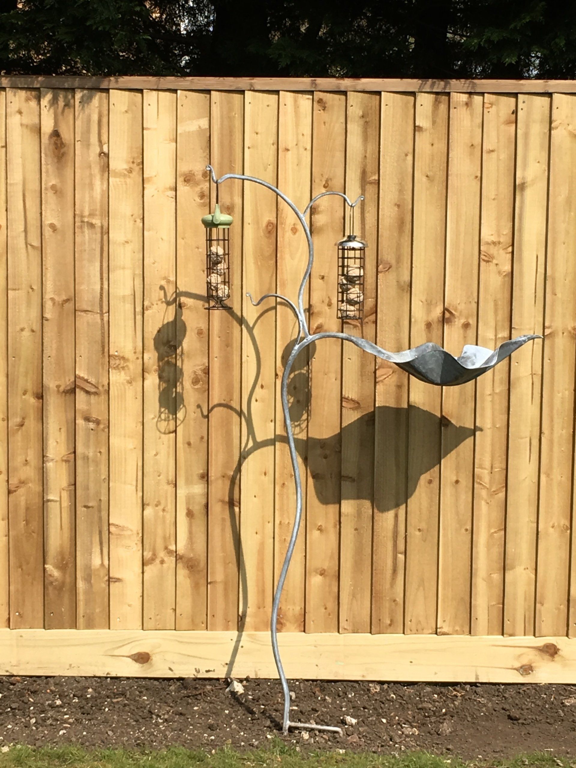 A bird feeder is sitting in front of a wooden fence.